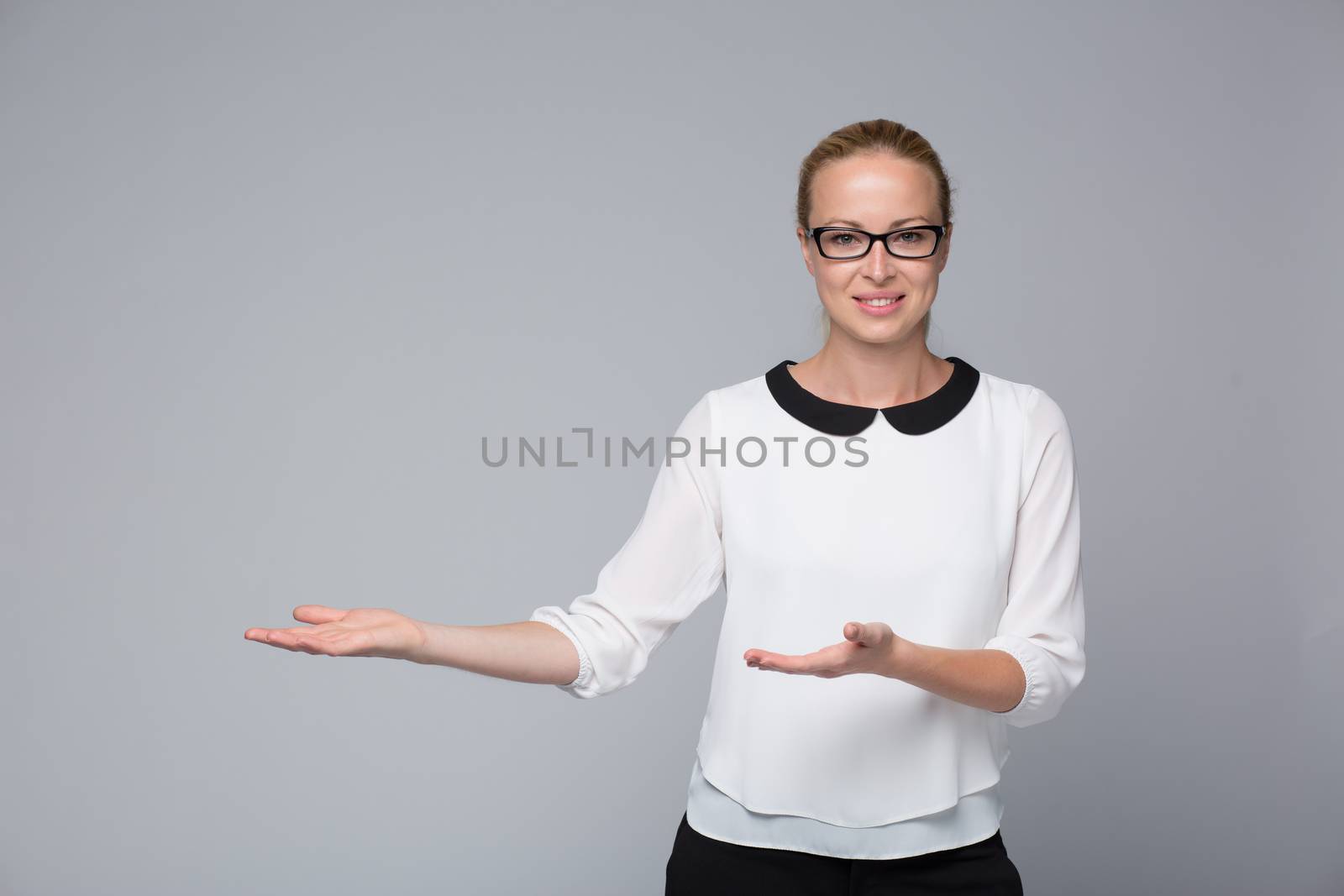 Beautiful young businesswoman smiling, holding open palm with empty copy space. Business woman showing hand sign to side, concept of advertisement product. Grey background.