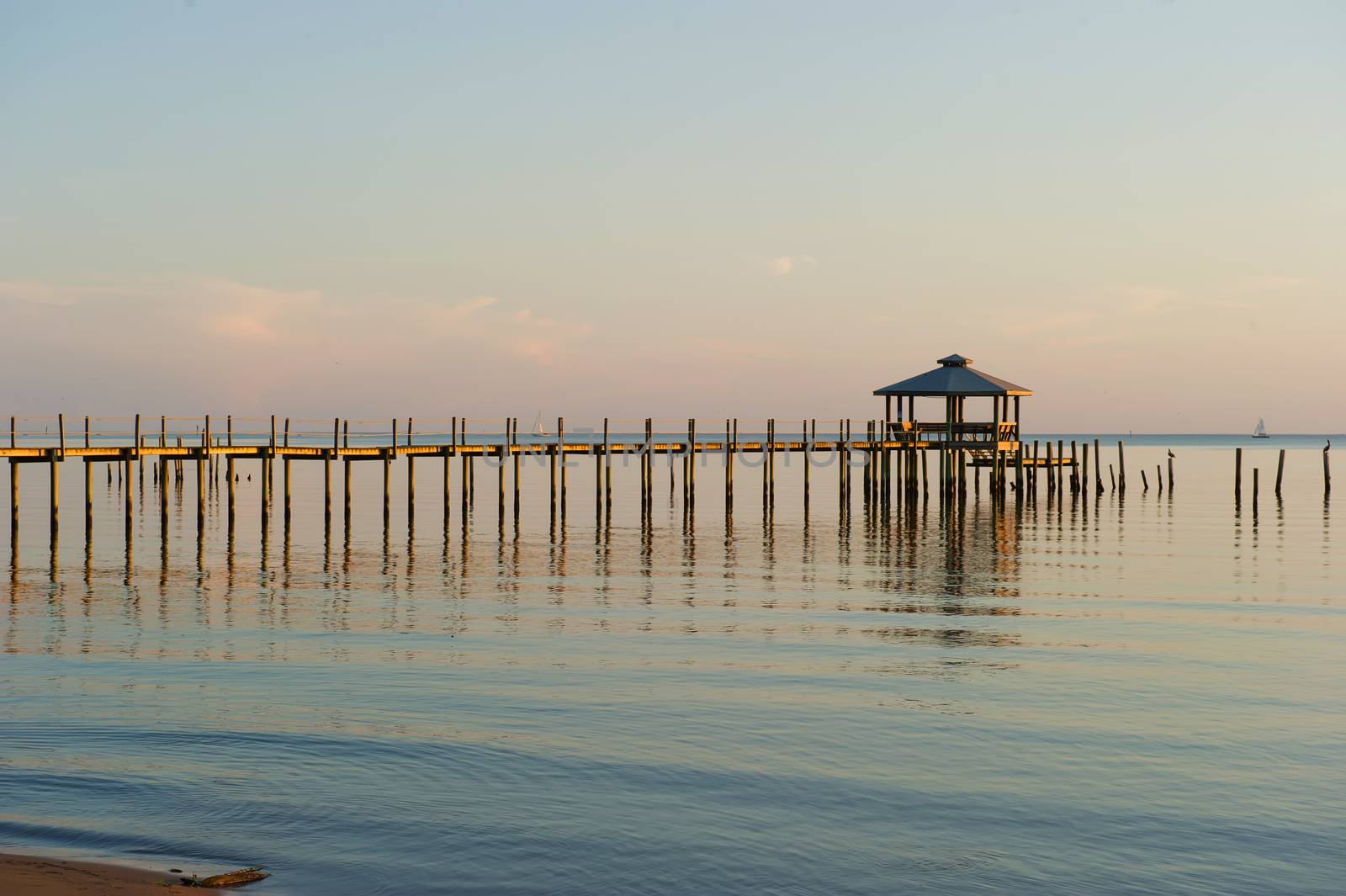 Late Evening Shot of Pier on Bay with calm water and sailboat in the distance