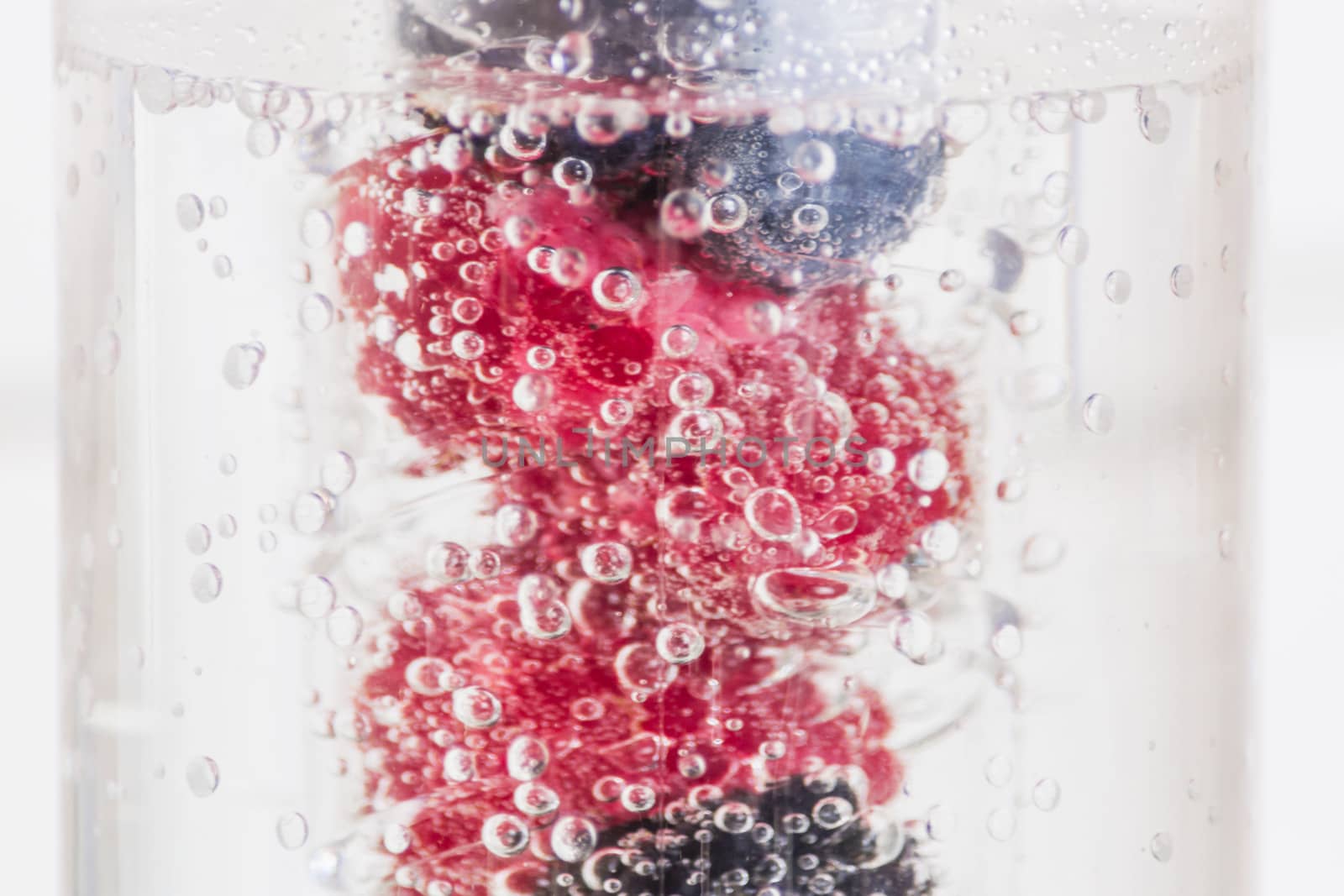 Berry fruits raspberries and blackberries in a row in a glass of mineral water.