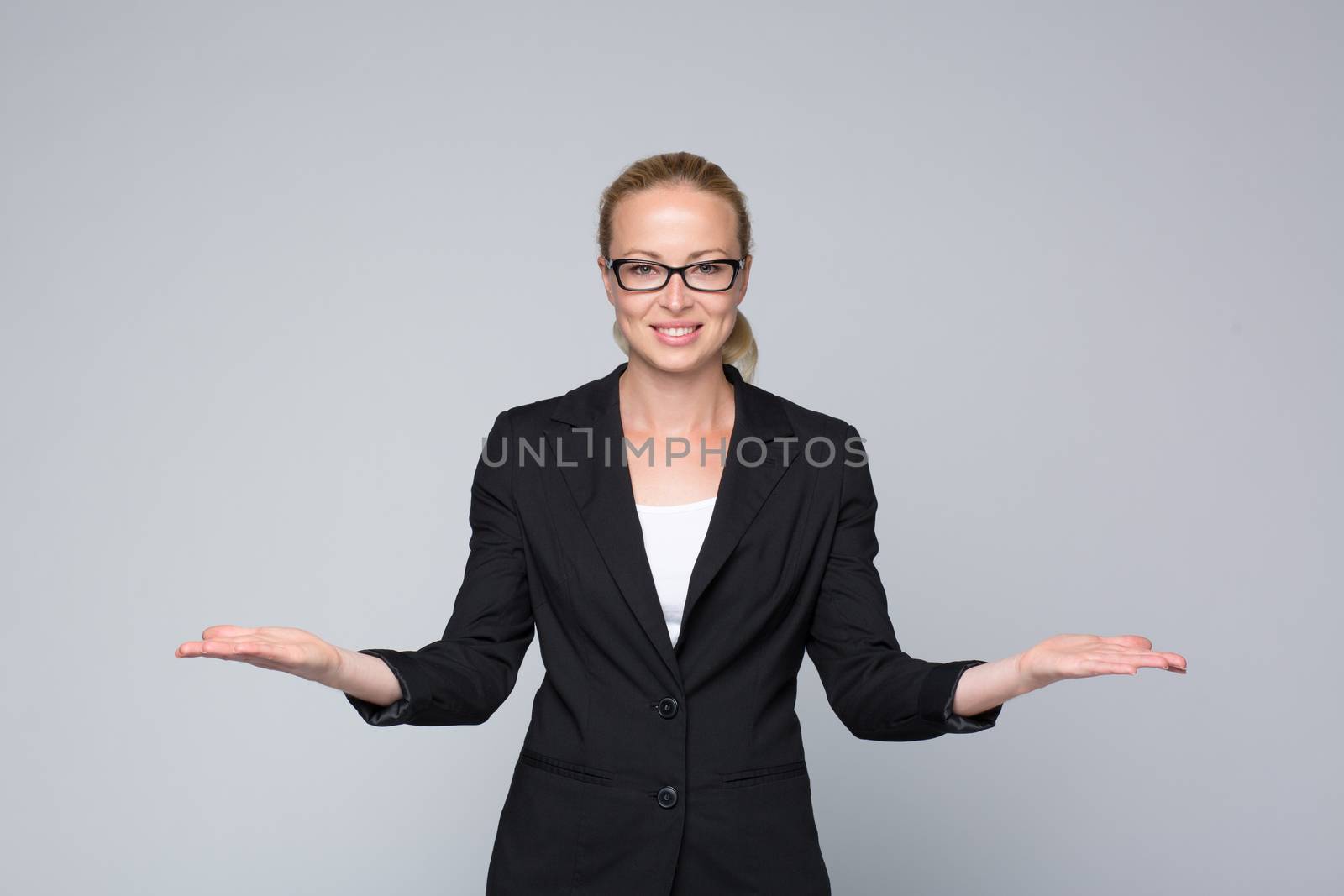 Beautiful young businesswoman smiling, holding open palms with empty copy space. Business woman showing hands sign to sides, concept of advertisement or comparing products. Grey background.