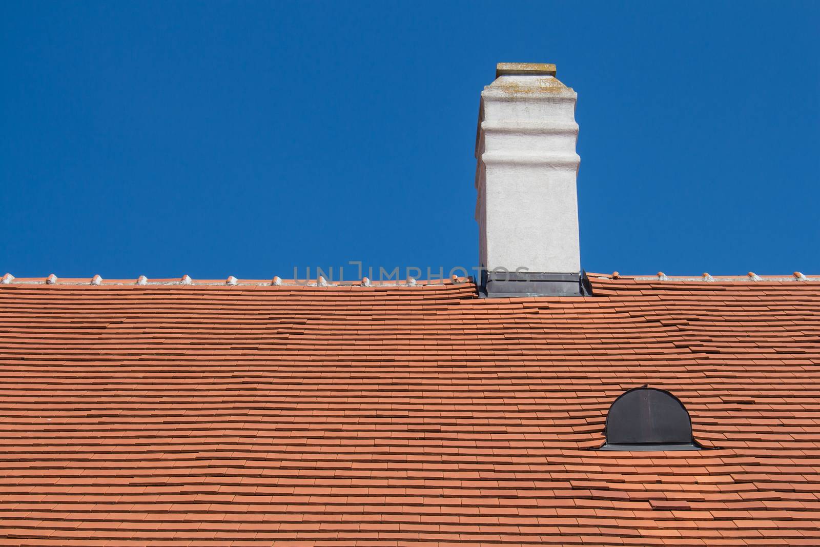 Old renewed orange roof with a white chimney and a roof window. Bright summer blue sky in the background.