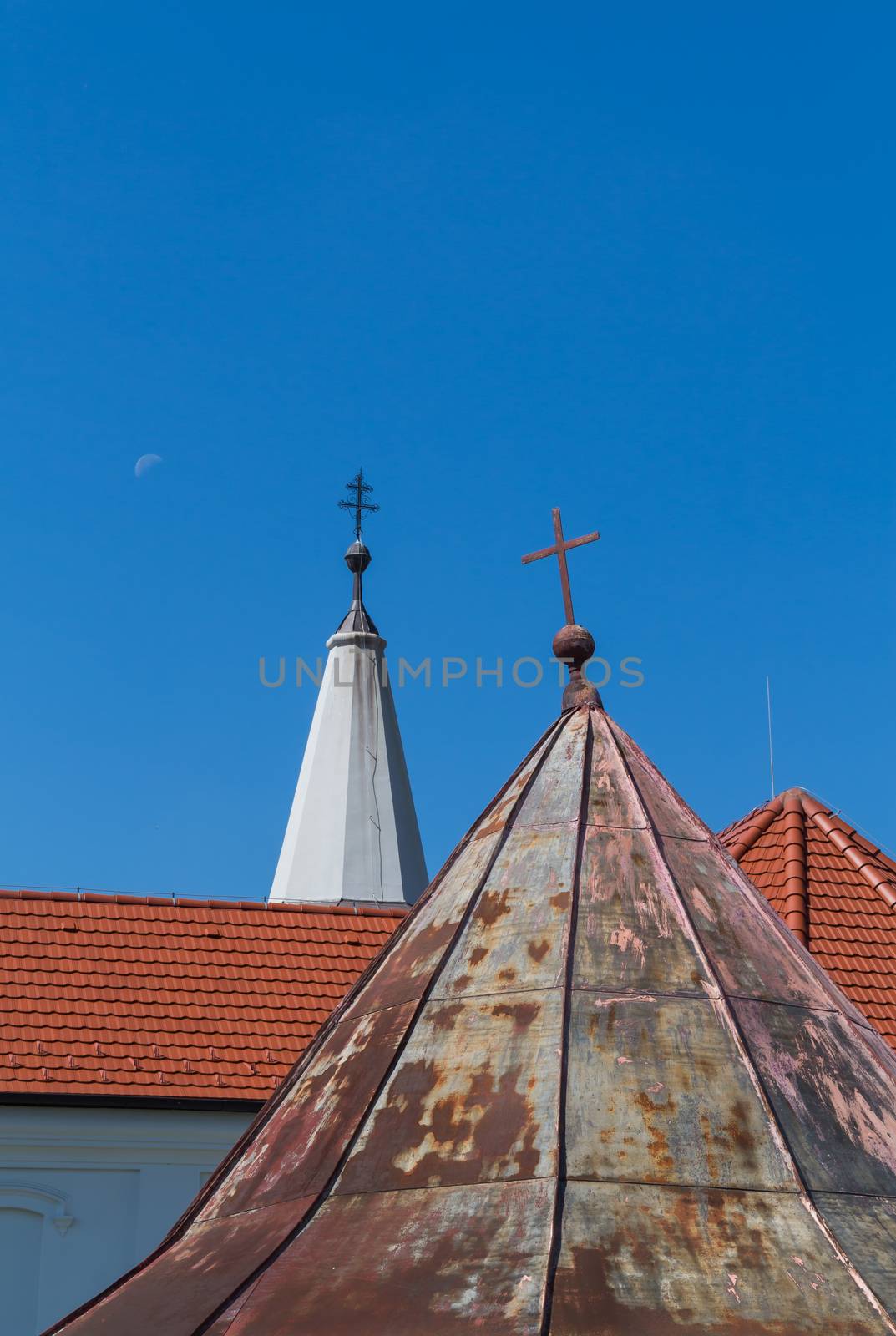 Older and new parts of the roofs of the church of Saint Peter and Paul in Cifer, Slovakia. Two crosses on the top of the towers. Blue sky with moon.