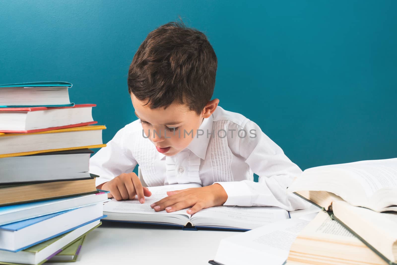 Сute boy reading book at the table, blue background