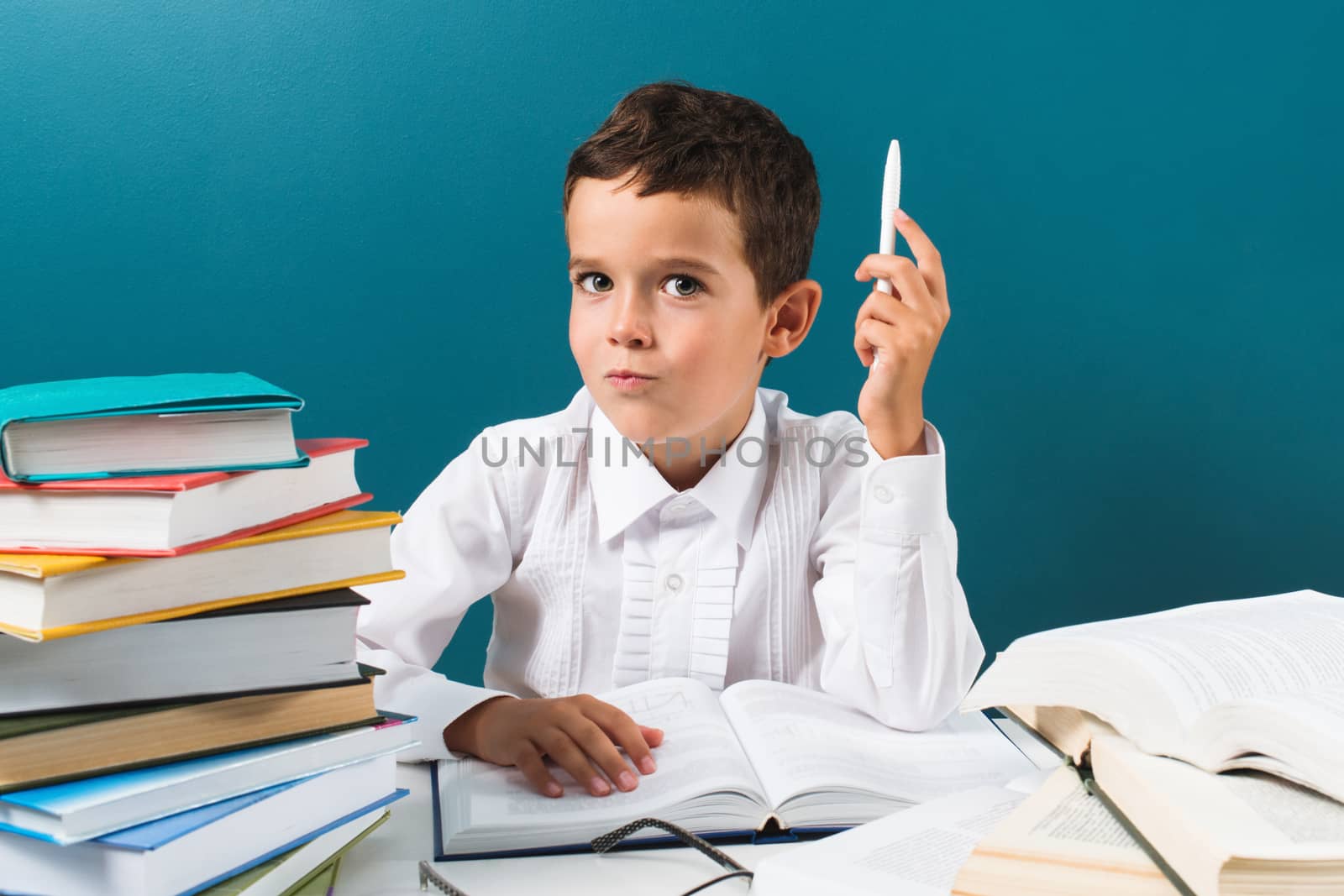 Contemplative cute little boy with books on the table