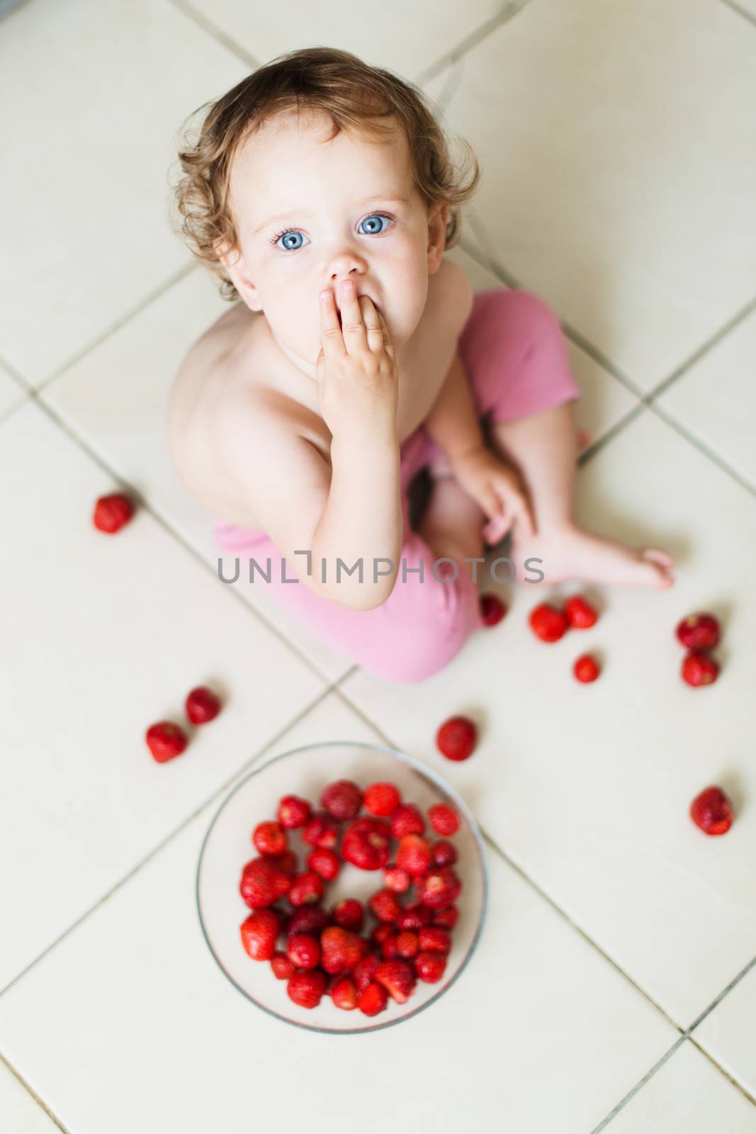 Cute little baby girl eats strawberries on the floor