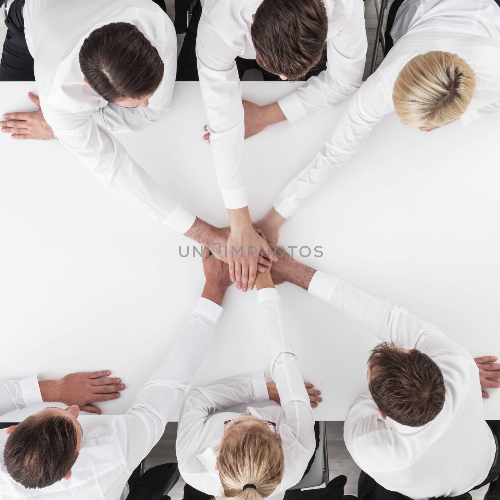 Business team stacking hands sitting around white table