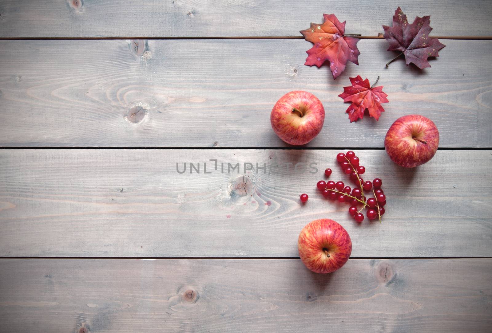 Red apples over a wooden background with maple leaves 