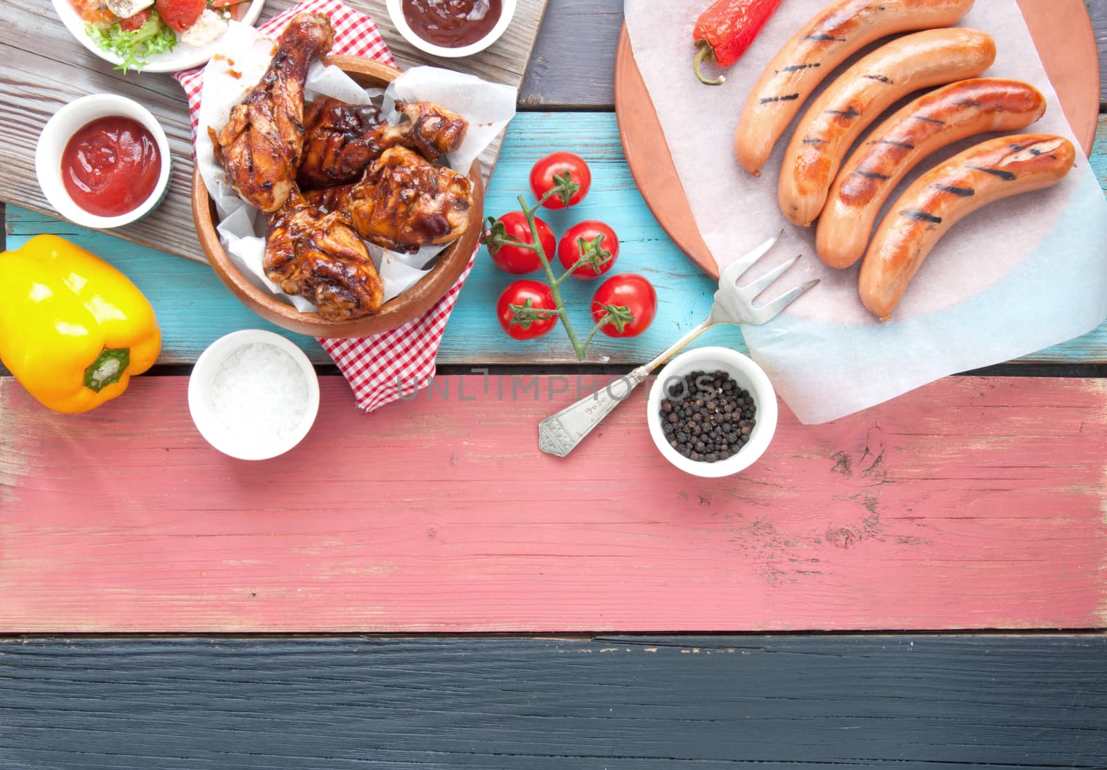 Selection of grilled barbecue meat including chicken and sausages with salad on top of a wooden table 