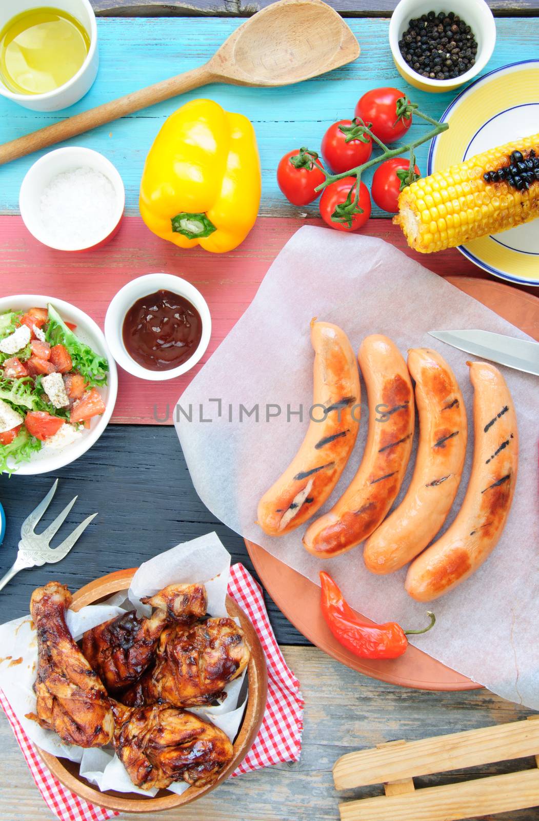Selection of grilled barbecue meat including chicken and sausages with salad on top of a wooden table