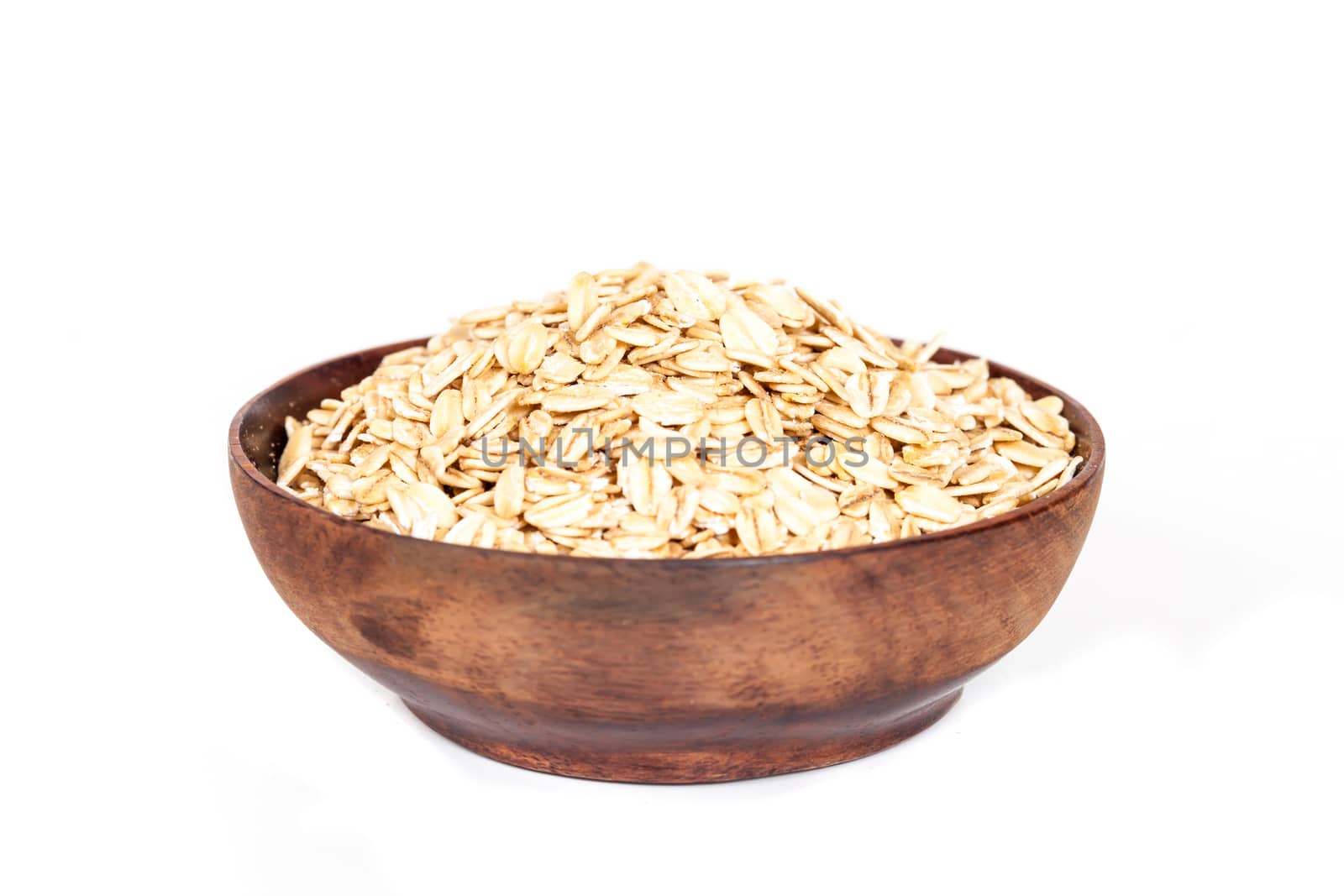 Wooden bowl with oats flakes pile on white background.