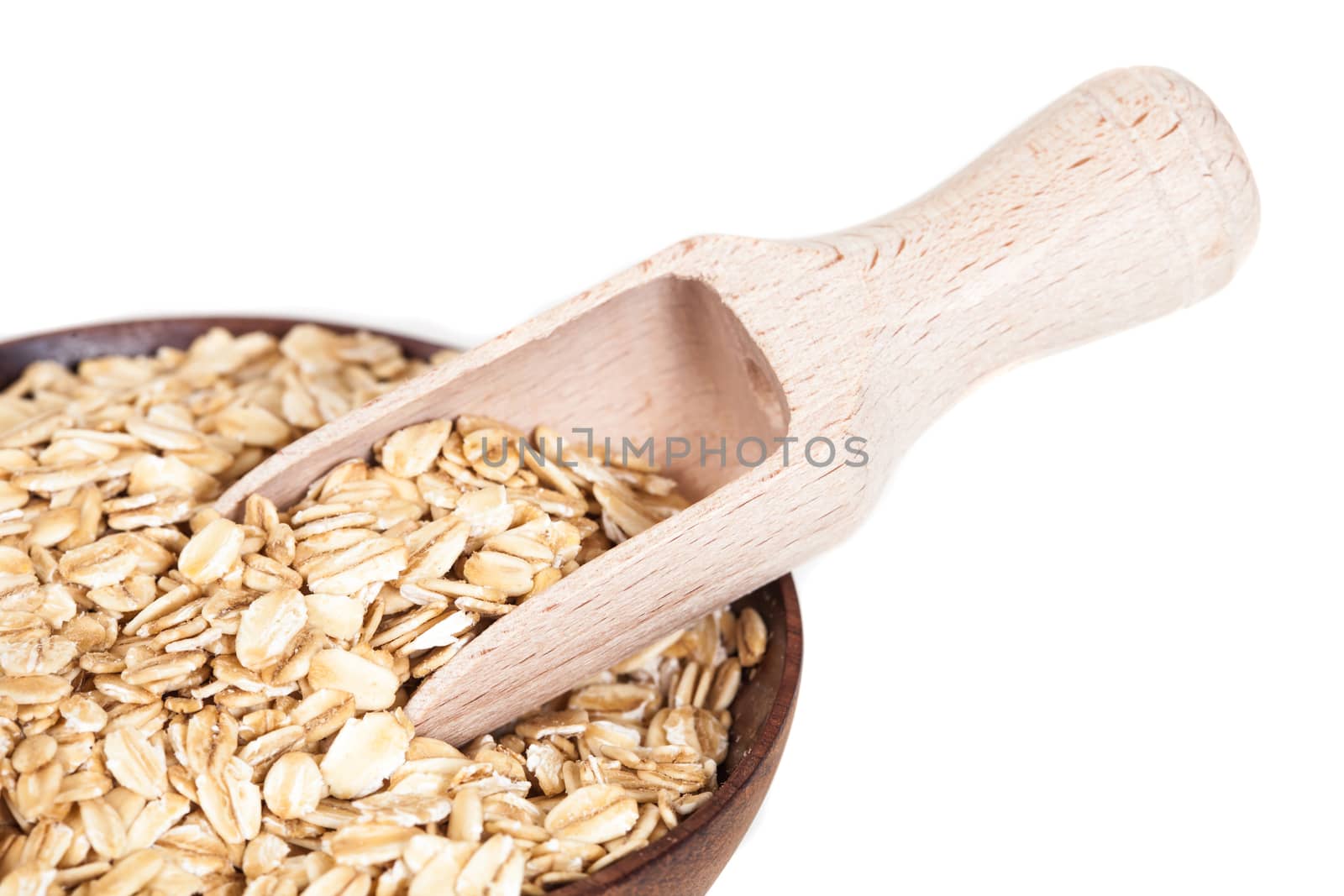 Wooden bowl with oats flakes pile on white background.