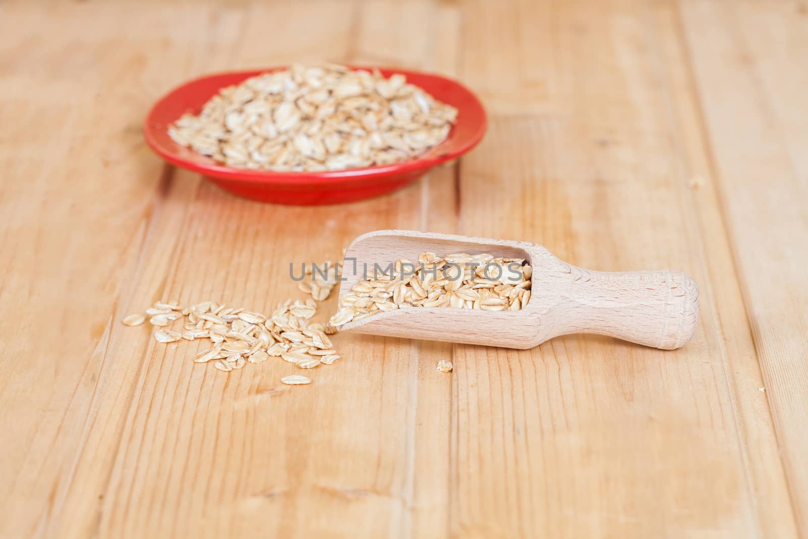 red dish and wood spoon with oats flakes pile on wood 
background.
