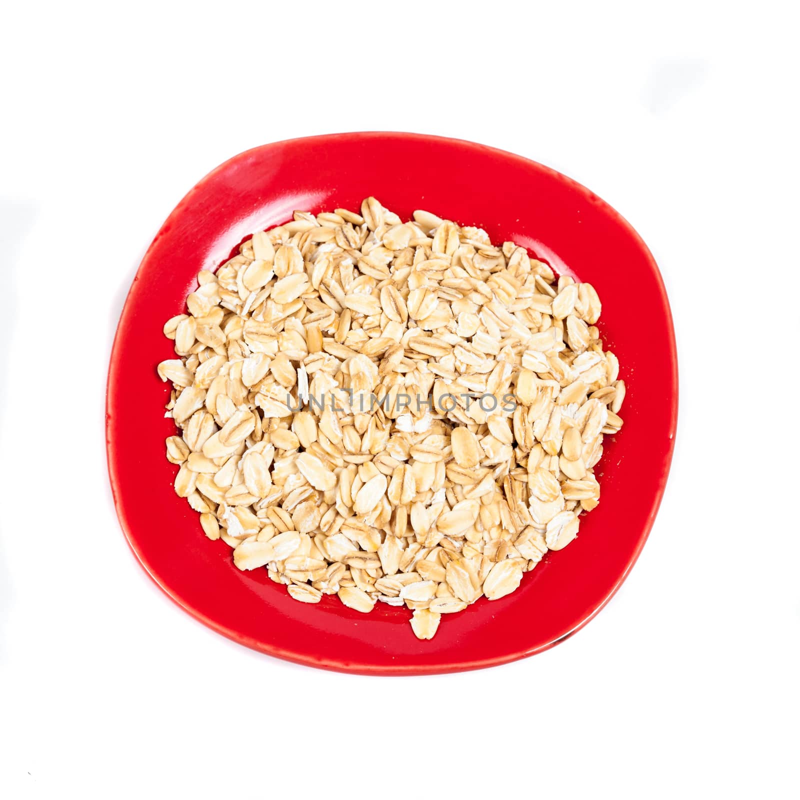 red dish  with oats flakes pile on white background. by amnarj2006