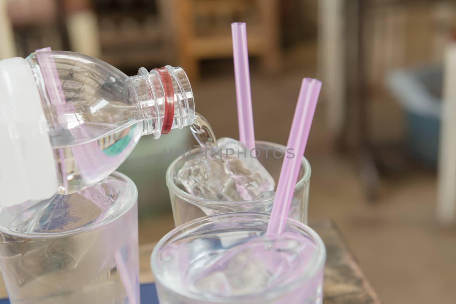 Water pouring on a plain glass with ice and pink straw. Selective focus.