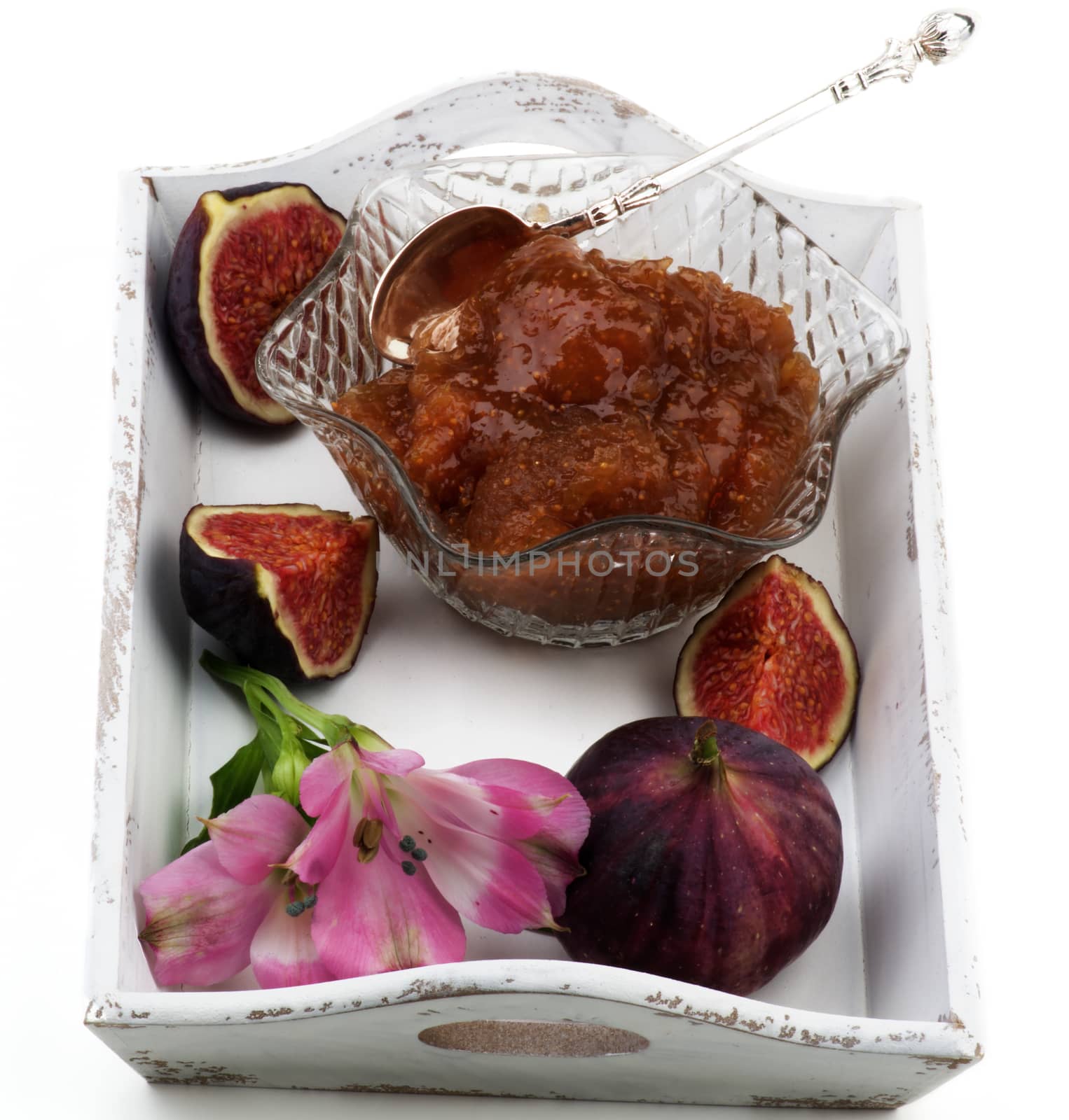 Delicious Homemade Fig Jam in Glass Kremanka with Fresh Fig Fruits and Flowers in White Wooden Tray isolated on White background