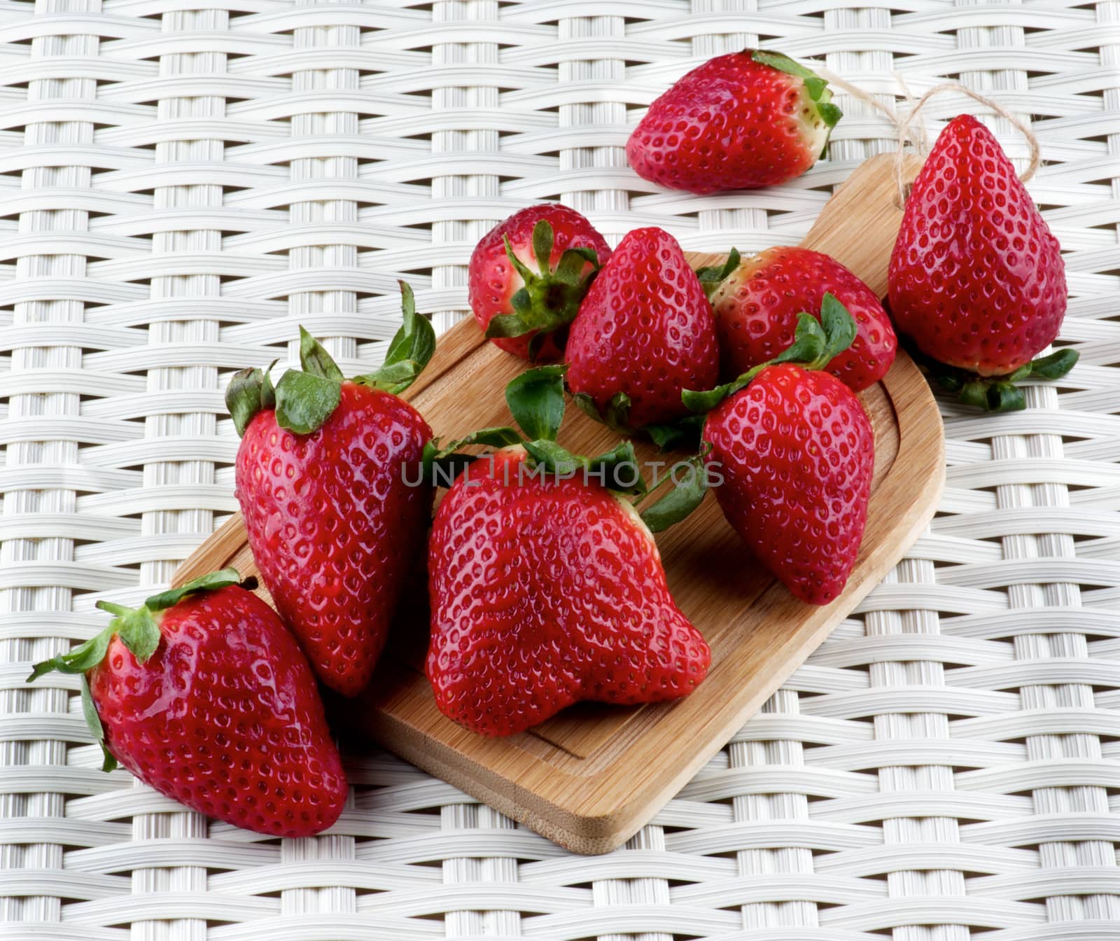 Heap of Fresh Ripe Strawberries on Small Wooden Cutting Board closeup on Wicker background