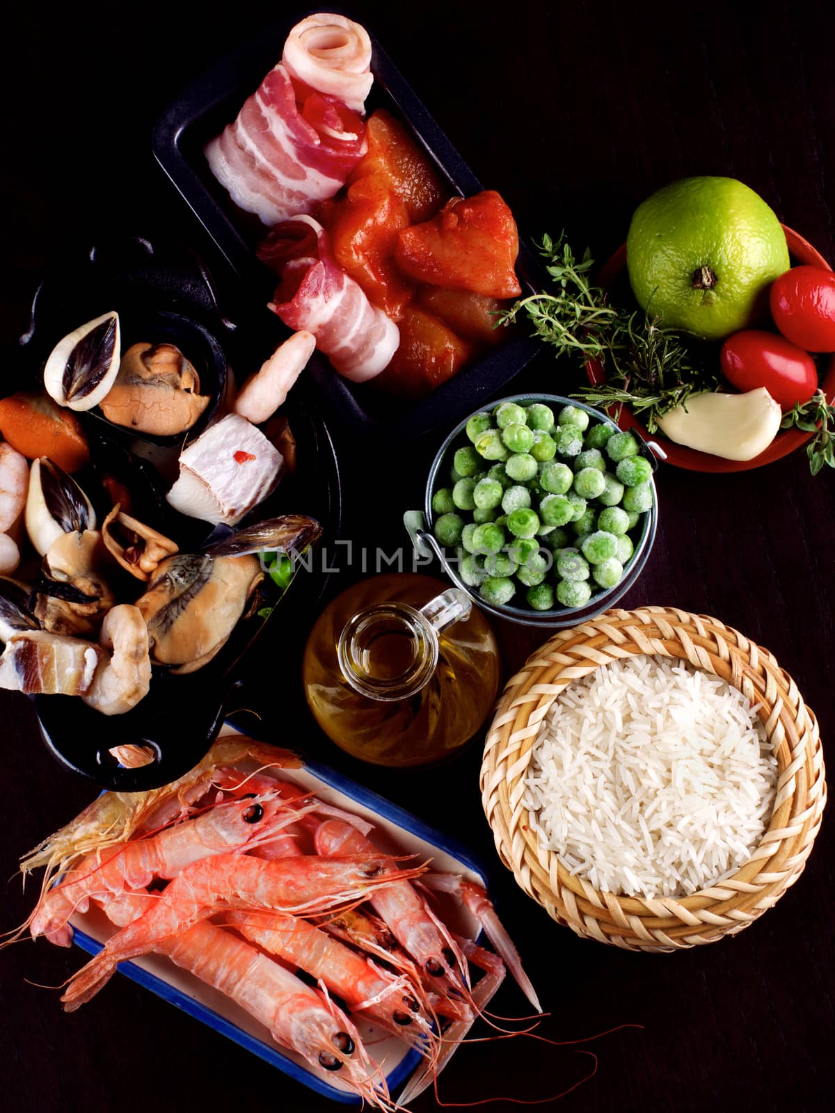 Arrangement of Raw Ingredients of Spanish Traditional Paella with Various Seafood, Mussels, Vegetables, Rice and Olive Oil closeup on Dark Wooden background. Top View