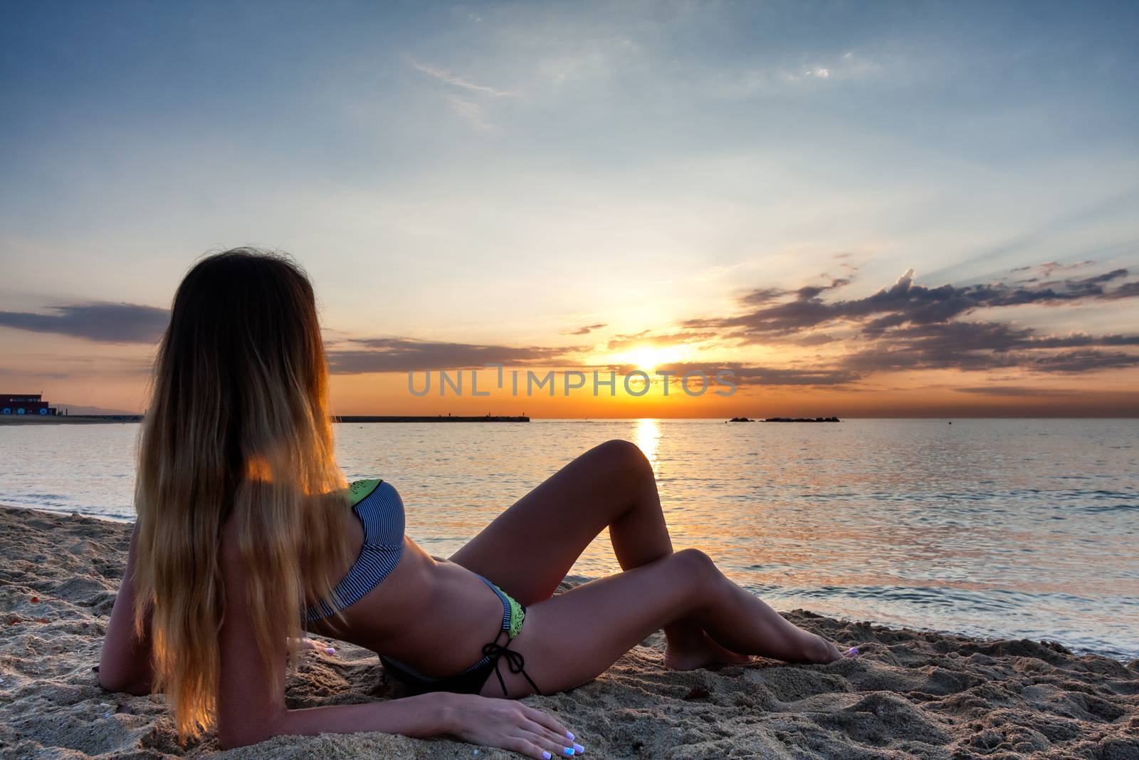 attractive sexy woman in bikini laying on sand on lonely beachon sunset sunrise