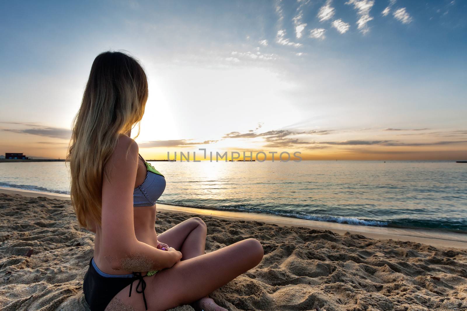 attractive sexy woman in bikini siting on sand on lonely beach on sunrise sunset