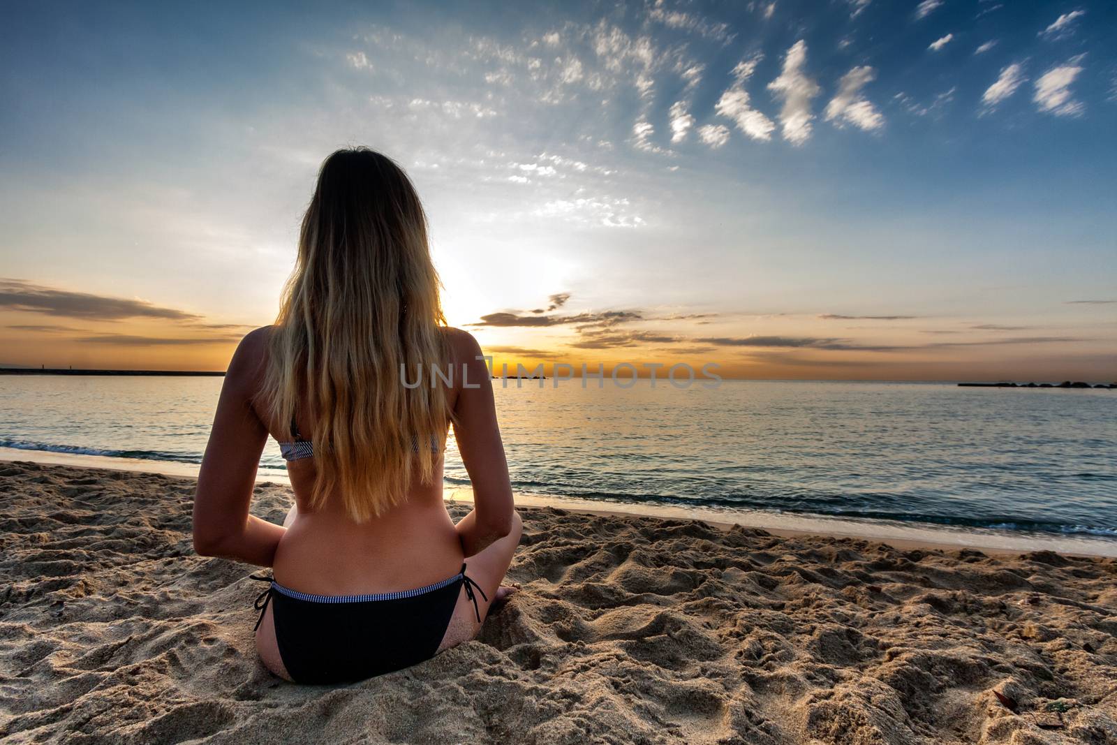 attractive sexy woman in bikini siting on sand on lonely beach on sunrise sunset