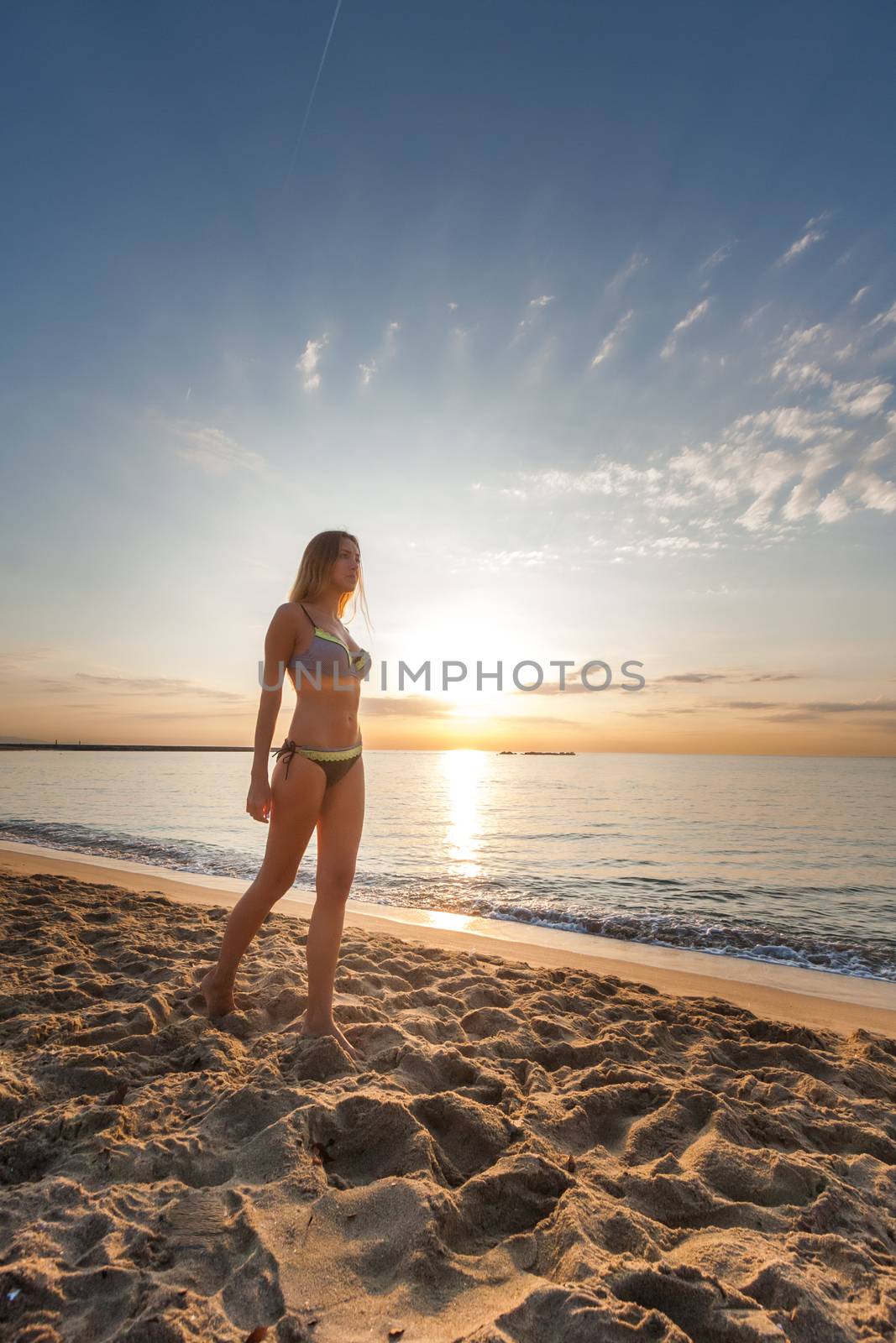 attractive sexy woman in bikini walking on sand on lonely beach on sunrise sunset