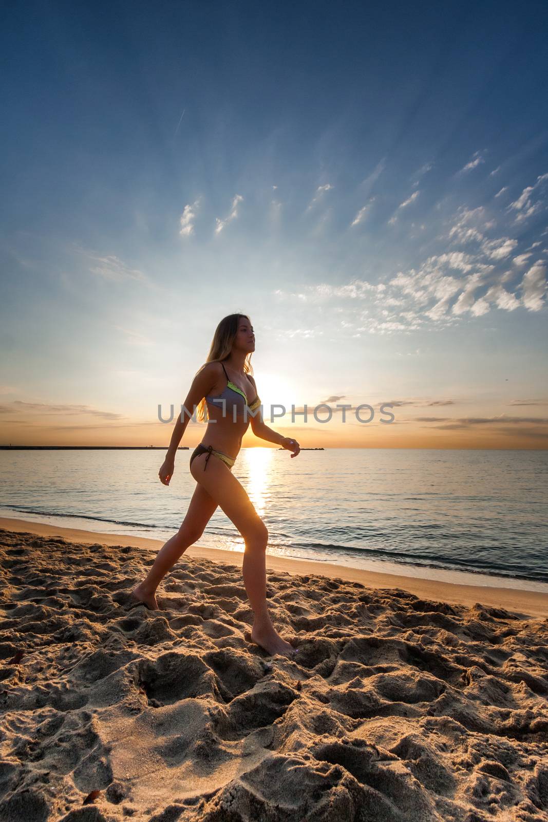 attractive sexy woman in bikini walking on sand on lonely beach on sunrise sunset