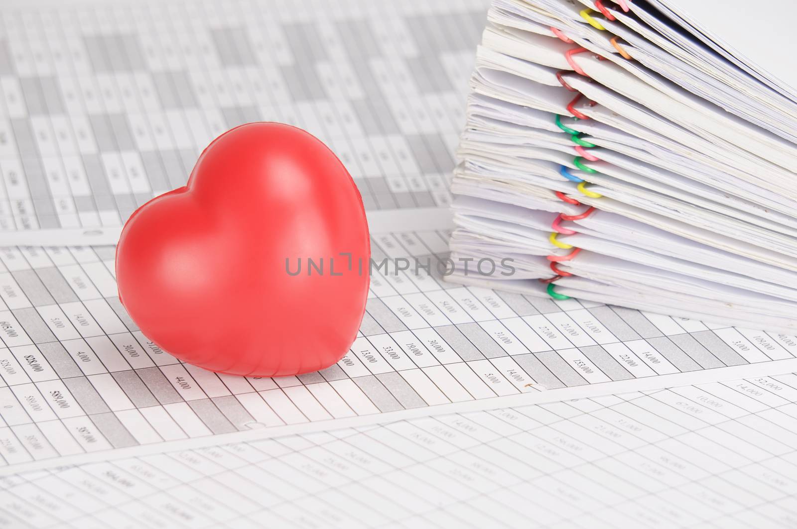 Red heart on finance account have blur pile overload paperwork of receipt and report with colorful paperclip as background.