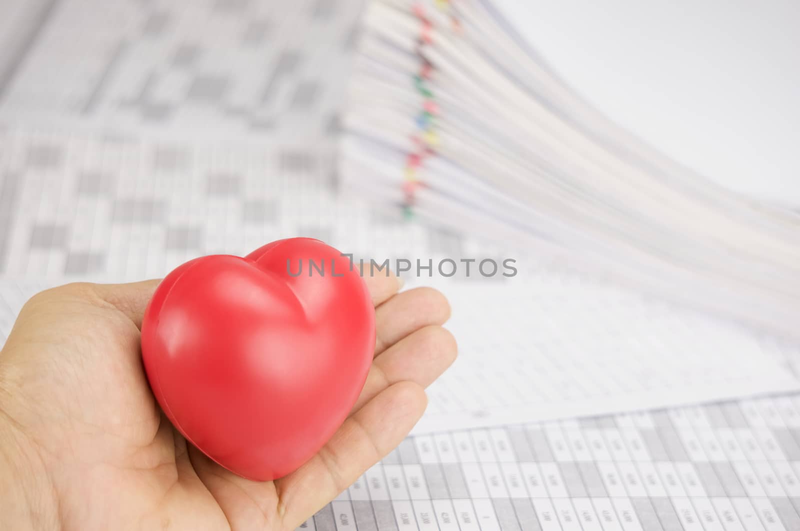 Red heart in hand have blur pile paperwork as background by eaglesky