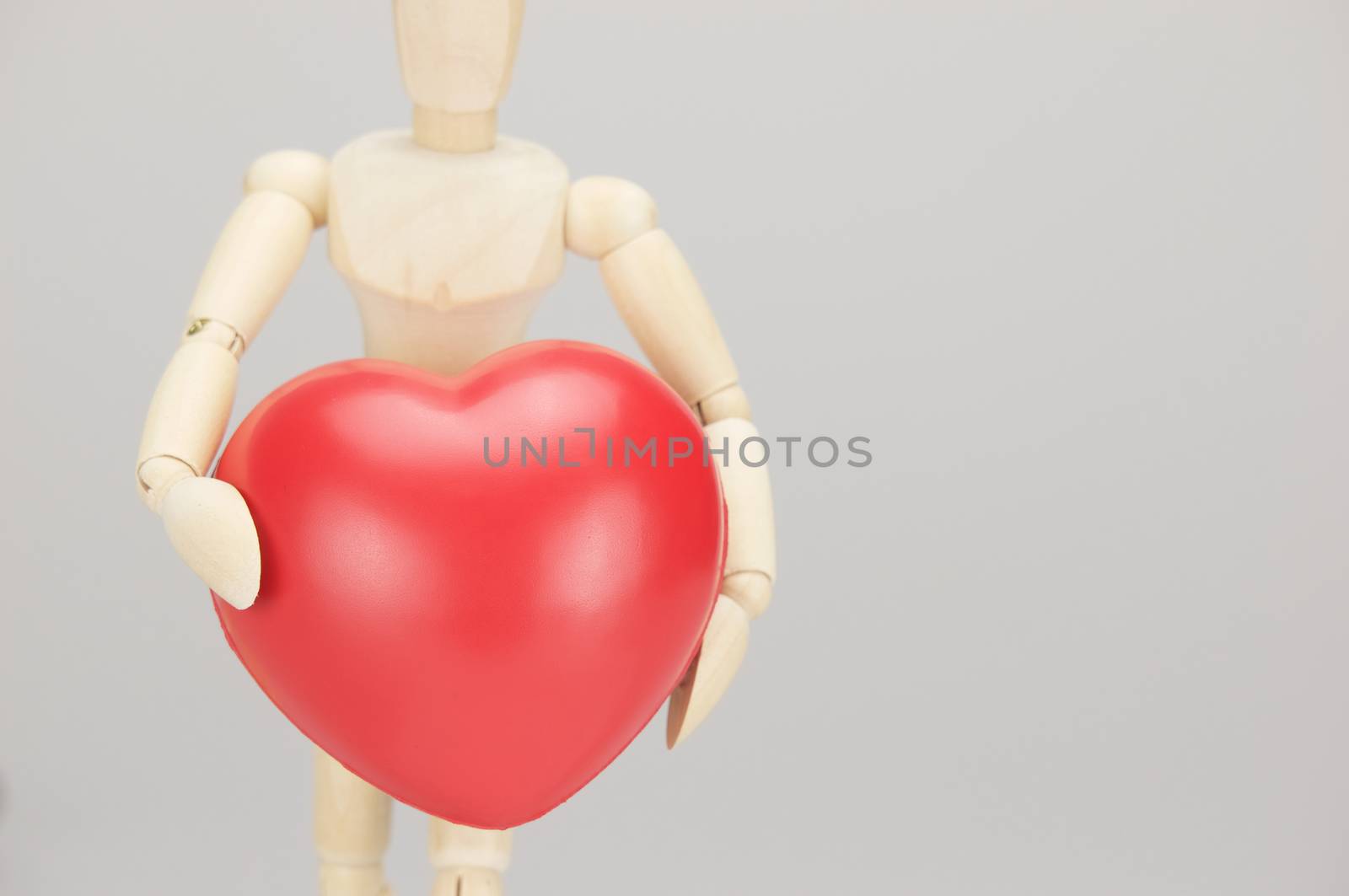 Wooden dummy holding red heart on left with white background.