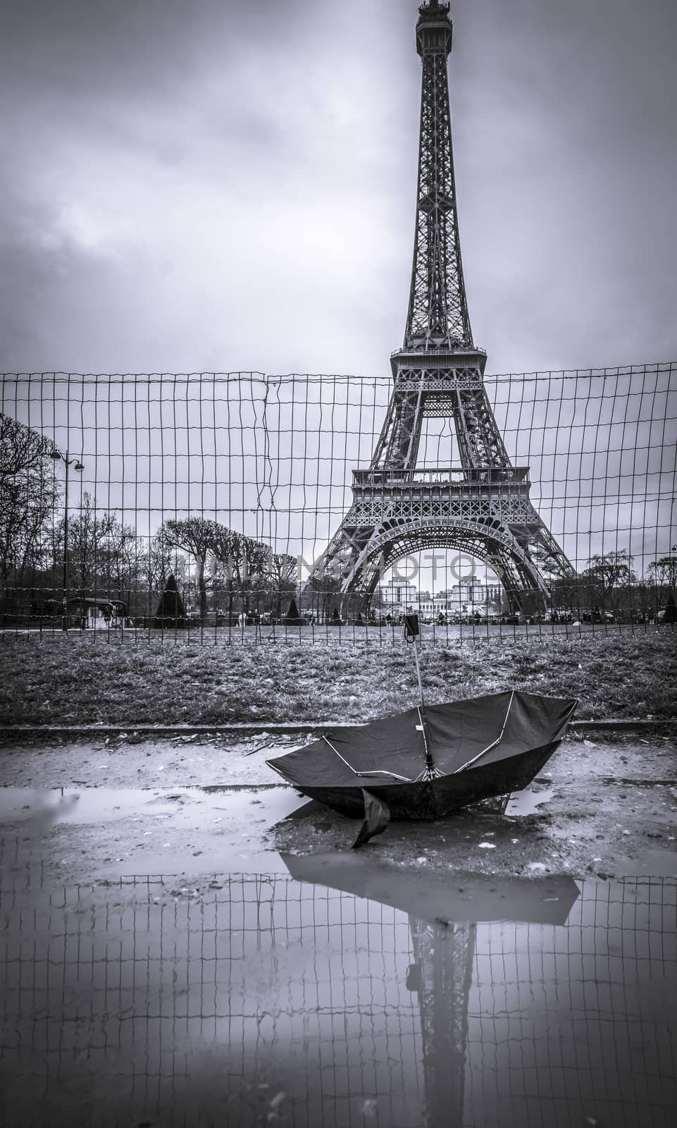 Monochrome image with Eiffel Tower on  a rainy day and an upside down umbrella in a puddle in foreground. Picture captured in Paris, France