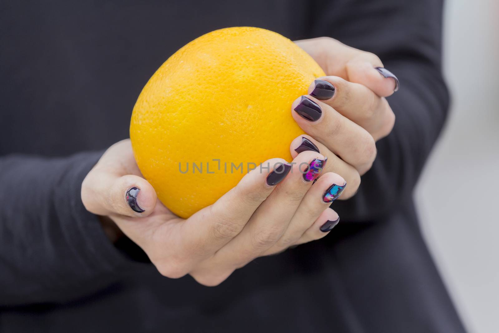 Bright, fresh orange in the hands of the girl with the fashionable manicure