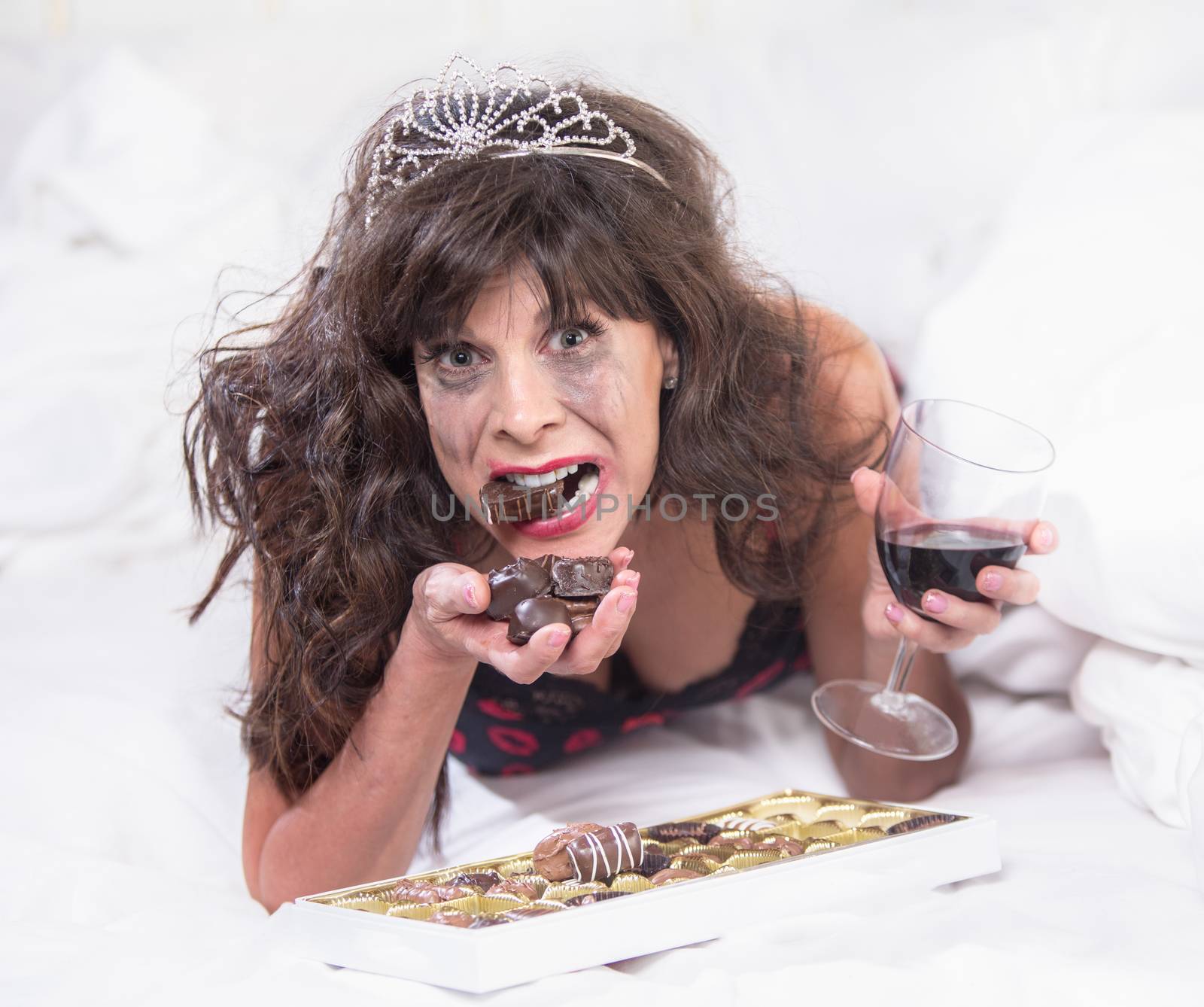 Mature woman wearing a tiara crying and cramming down chocolates in her bedroom