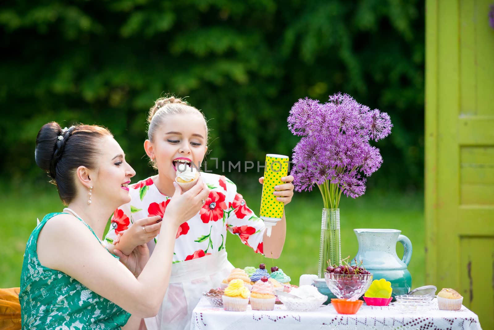 Young mother and her daughter cooking cupcakes together in the backyard