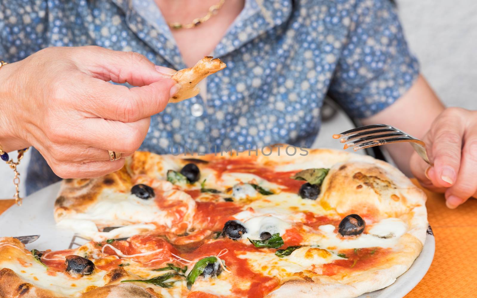 Close-up of woman hands cutting and eats pizza outside at restaurant, selective focus.