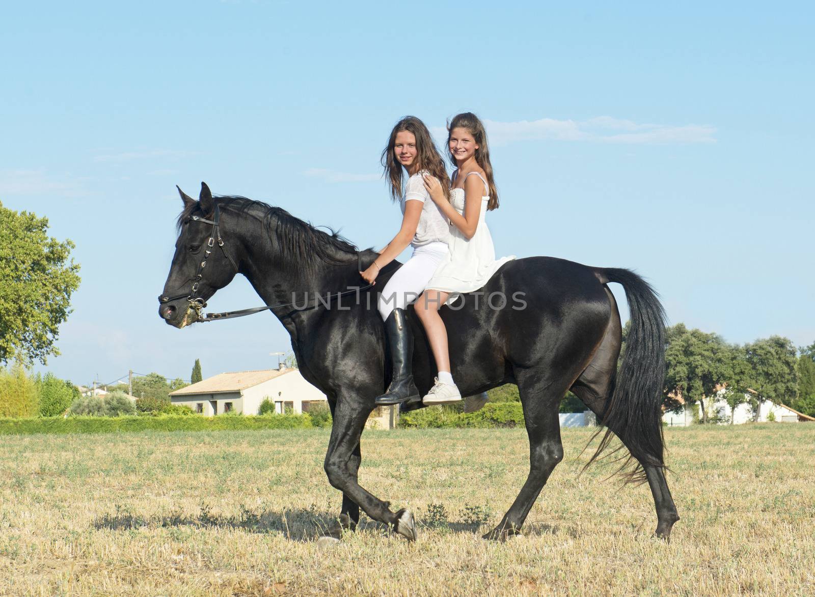 young girls riding a black stallion in a field