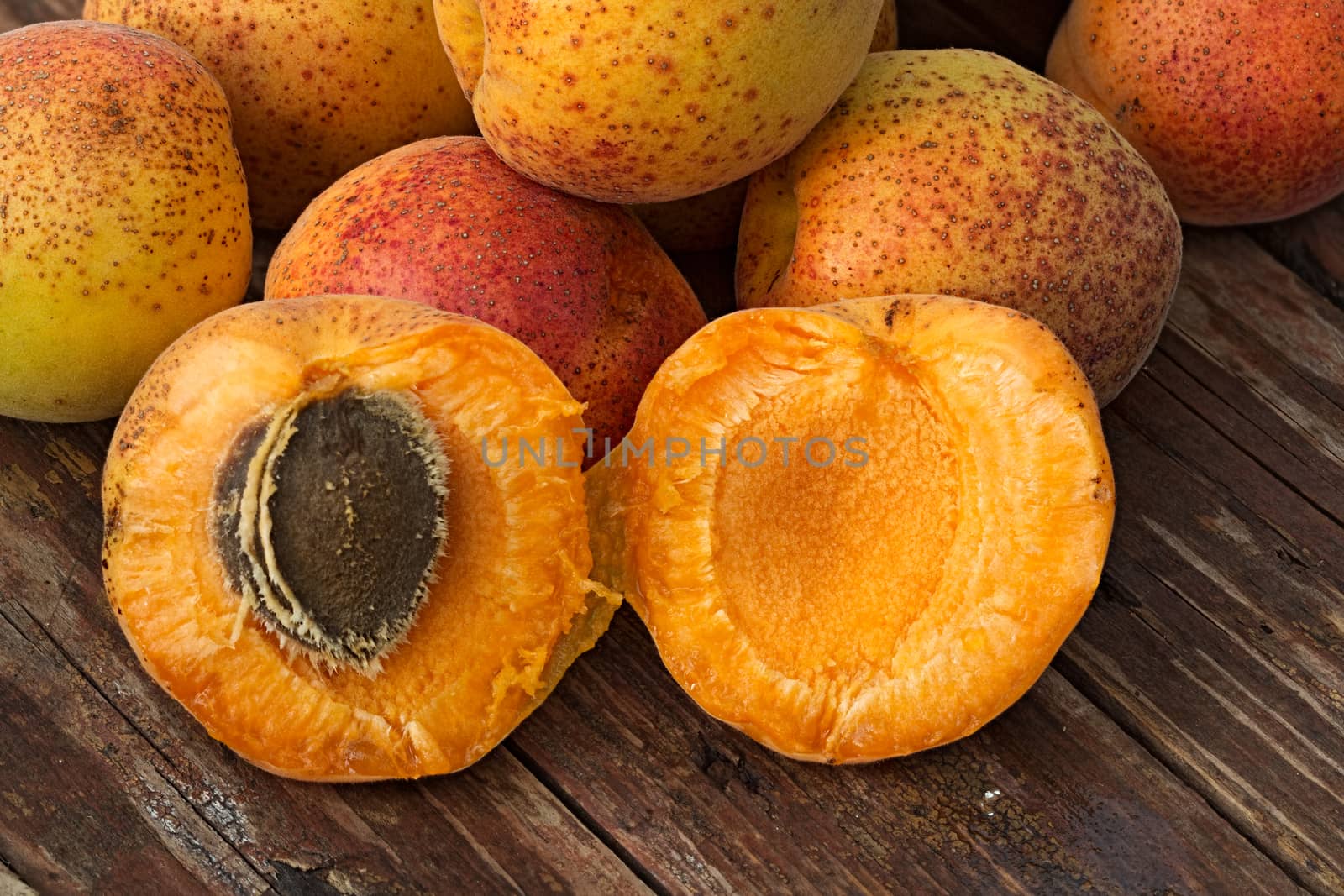 Few ripe orange whole apricots and one cut in half into a rough wooden background. Summer fruit background. Close-up image