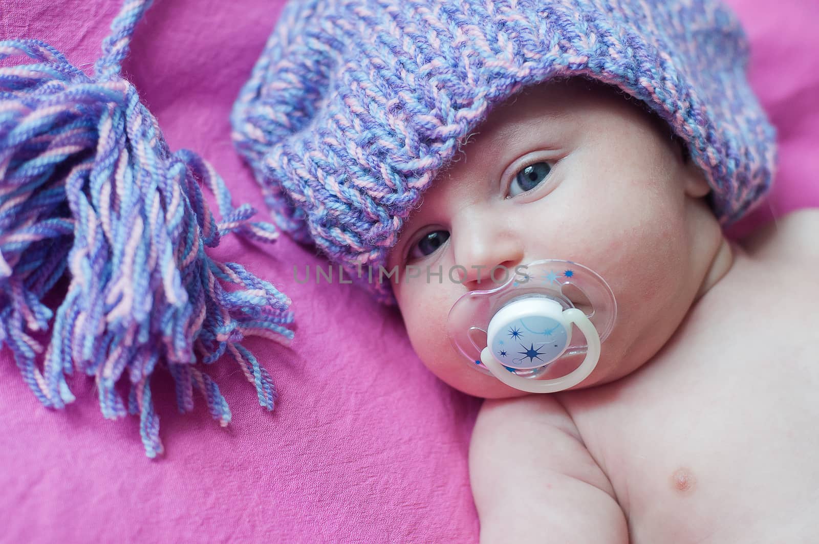 Little baby with soother in hat lays