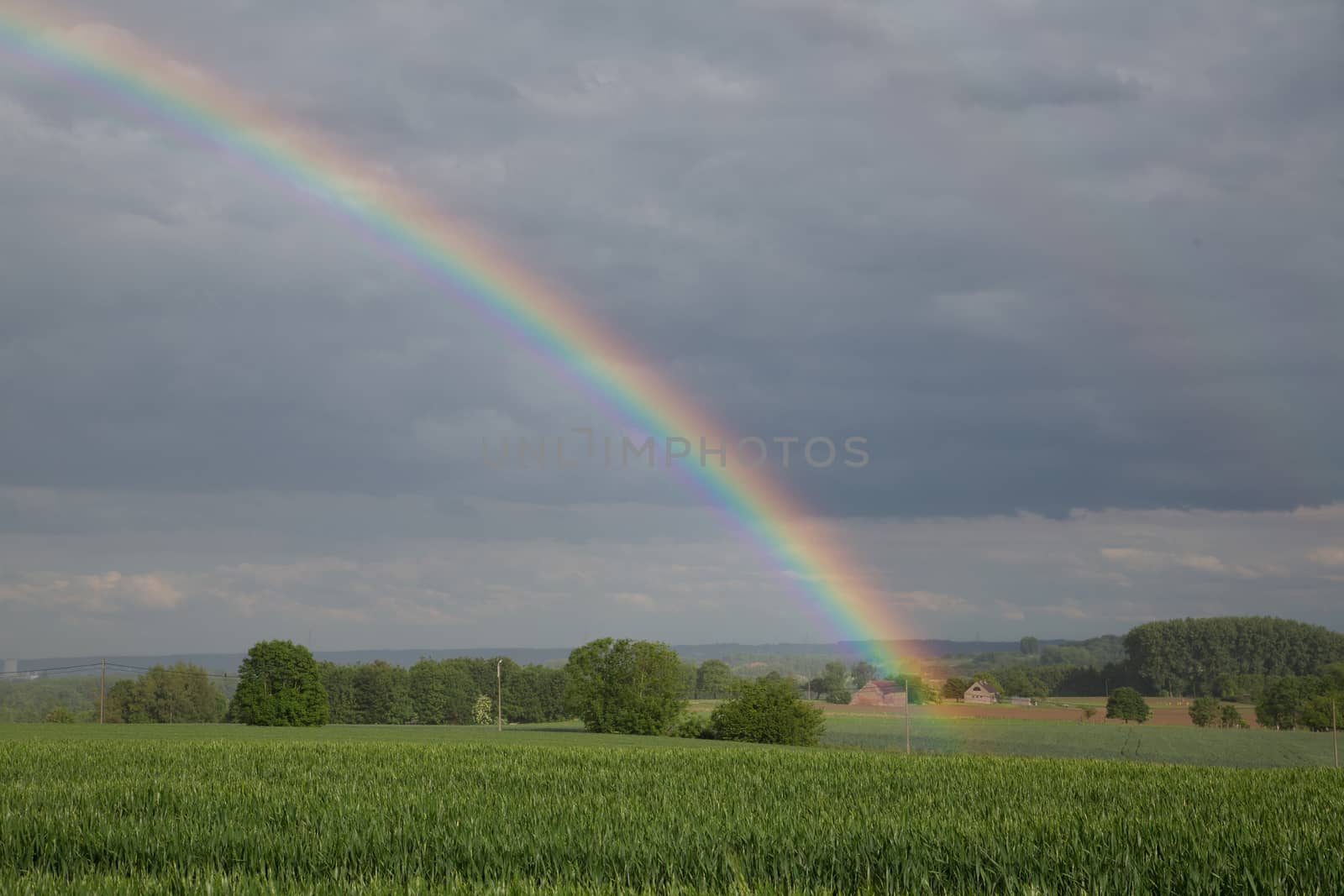 Natural rainbow over green field and dark sky