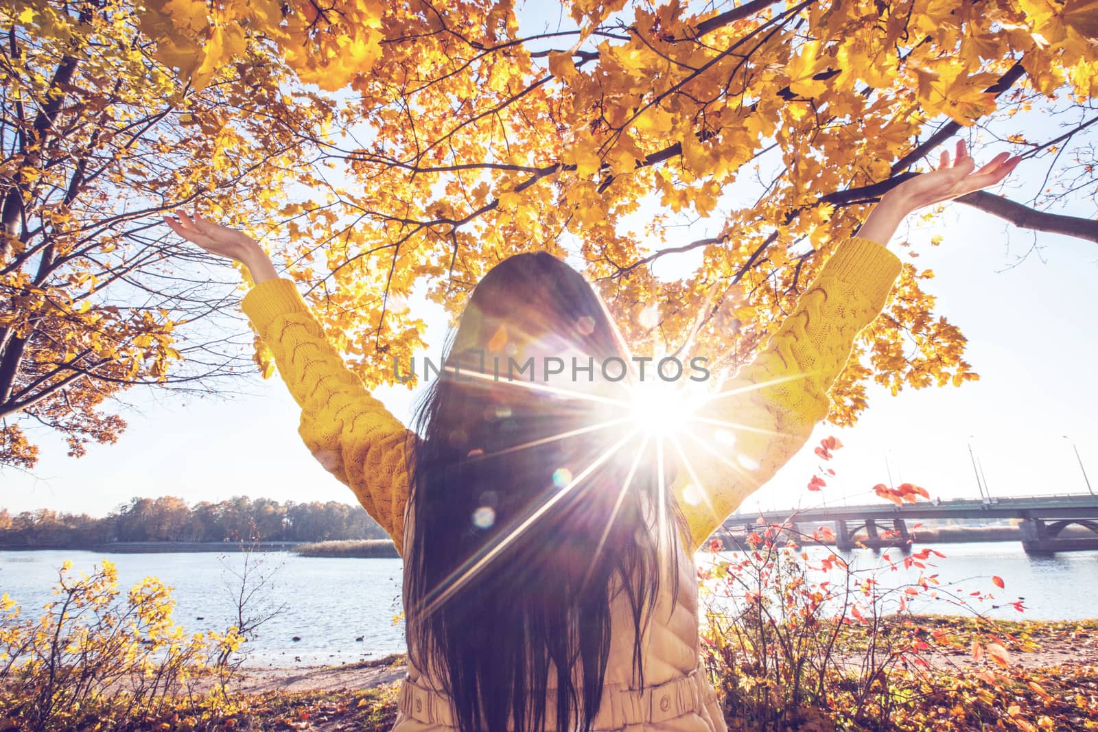 Happy woman with raised hands in sunny autumn park