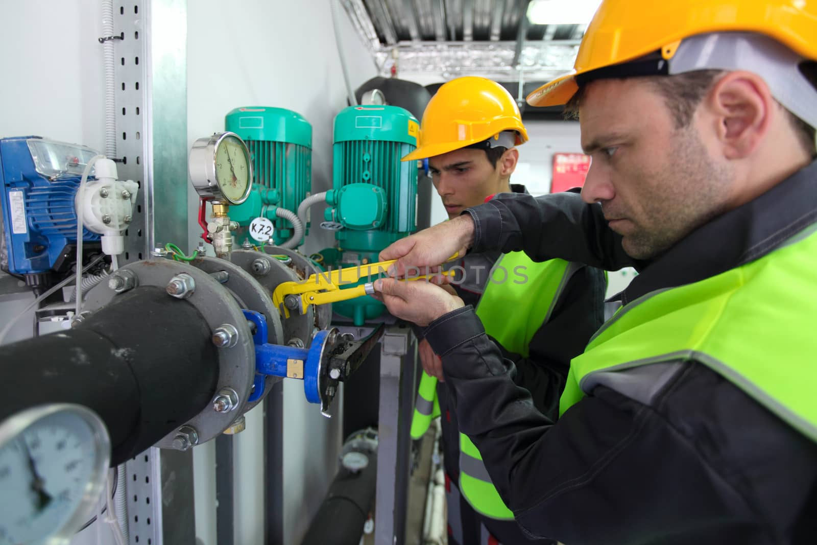 Two workers in hardhats at plant checking parameters of pressure