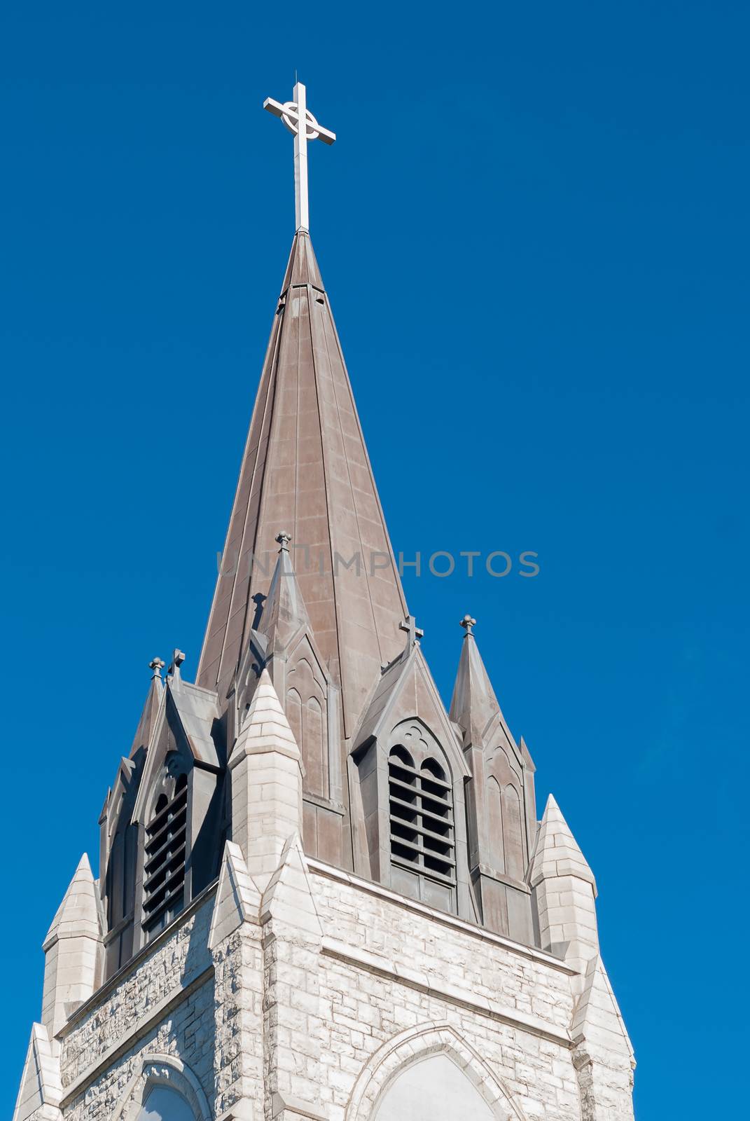 Steeple on top of a white stone church with a blue sky background.