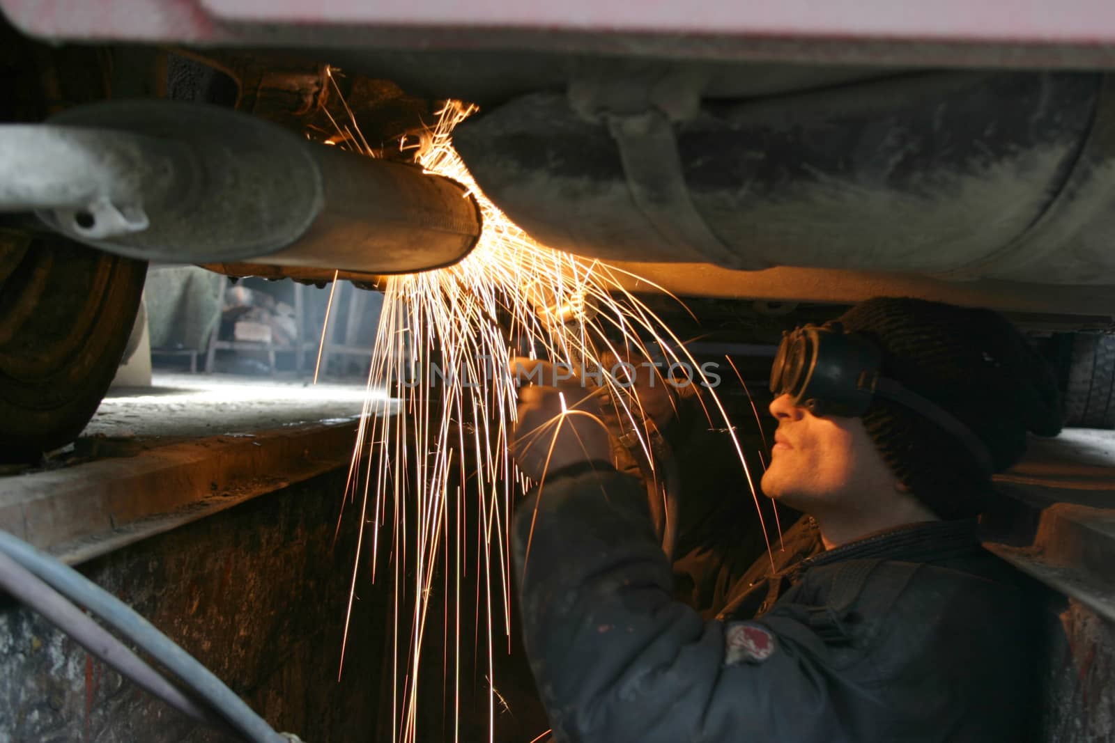 Welder and fire sparkles, working under a car.