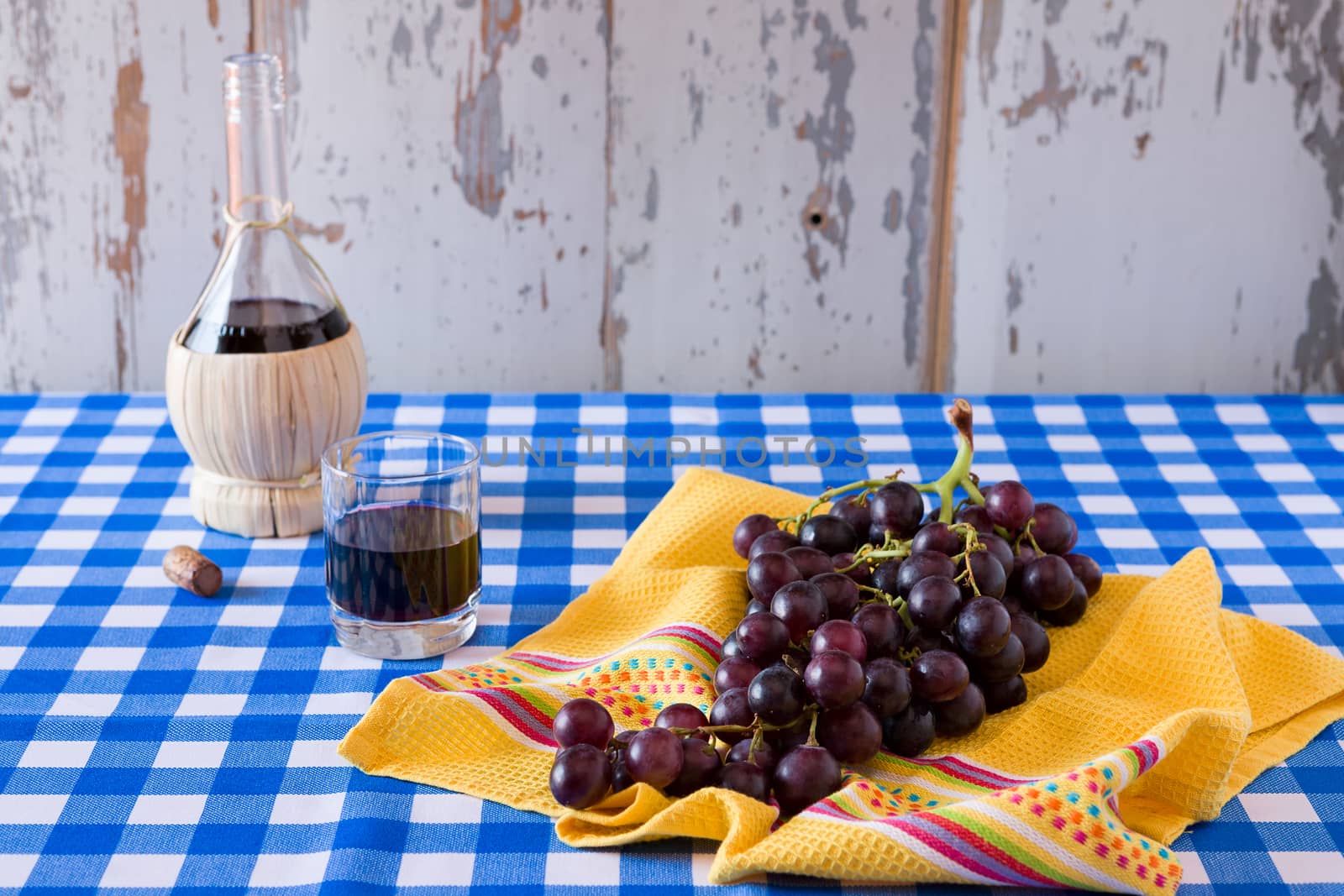 Bunch of red grapes and a glass of red wine with a wine flask on a checkered tablecloth