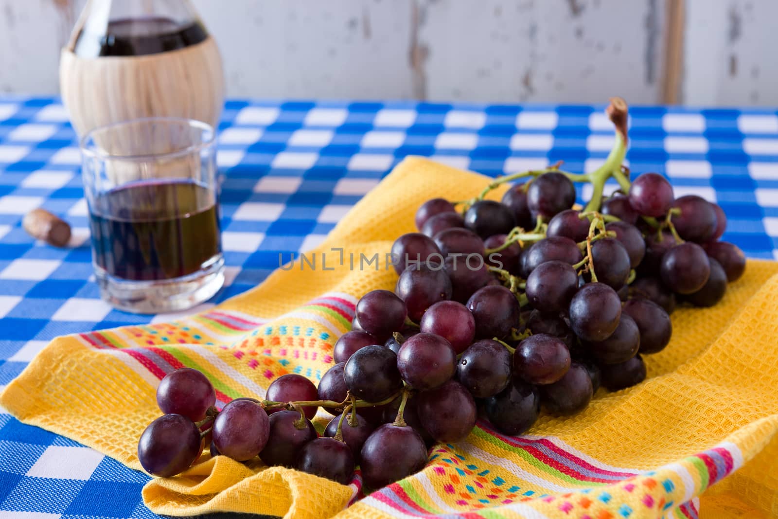 Closeup of a bunch of red grapes and a glass of red wine on a checkered tablecloth