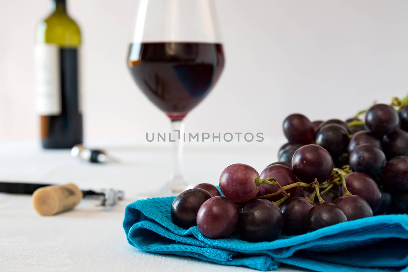 Closeup of a bunch of red grapes and a glass of red wine with a wine bottle on a blue tablecloth