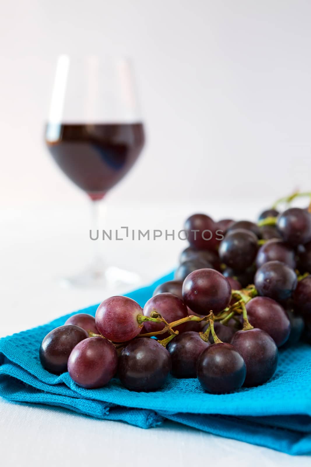 Closeup of a bunch of red grapes and a glass of red wine on background over a blue tablecloth