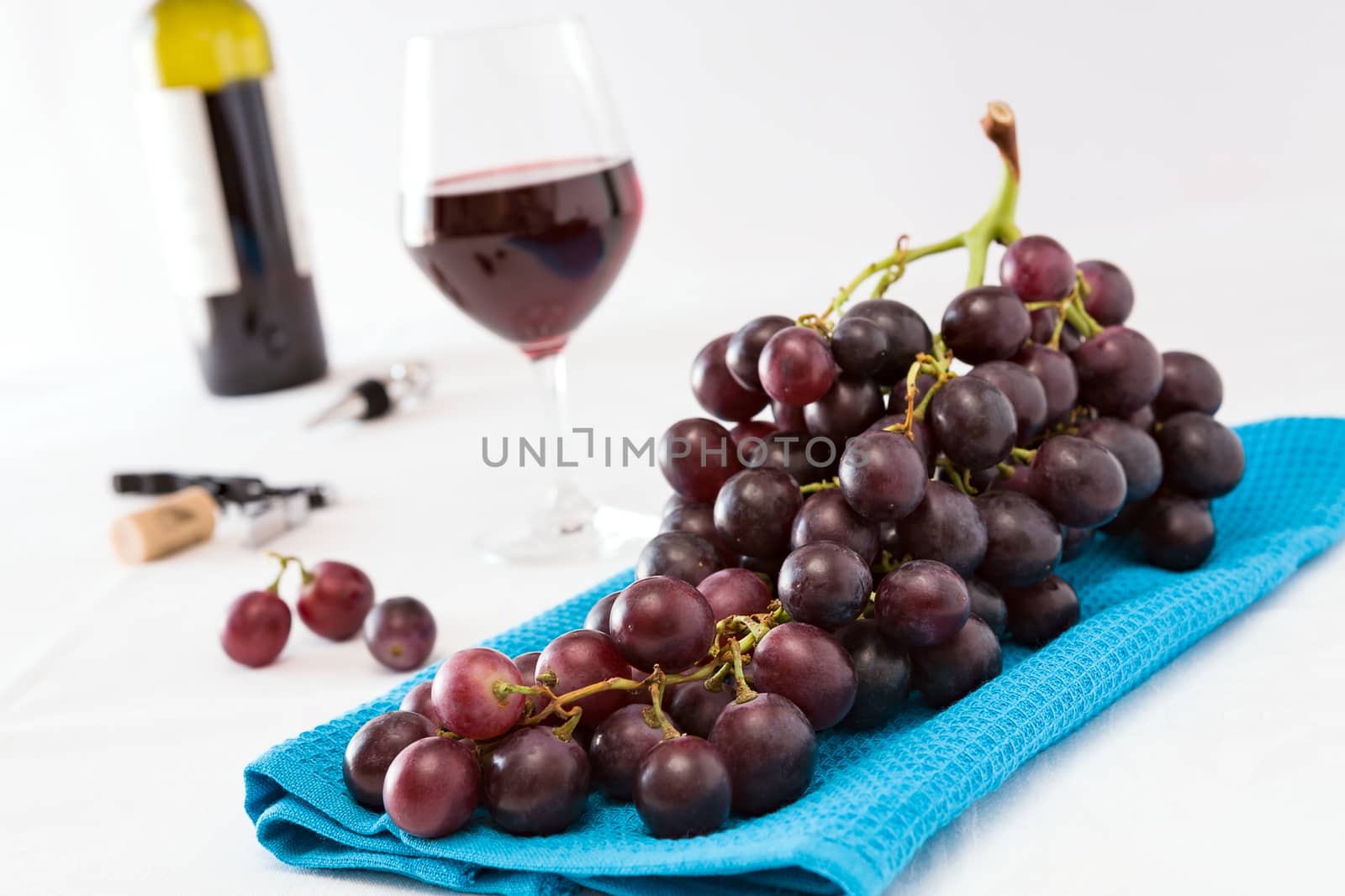 Closeup of a bunch of red grapes and a glass of red wine with a wine bottle on background over a blue tablecloth