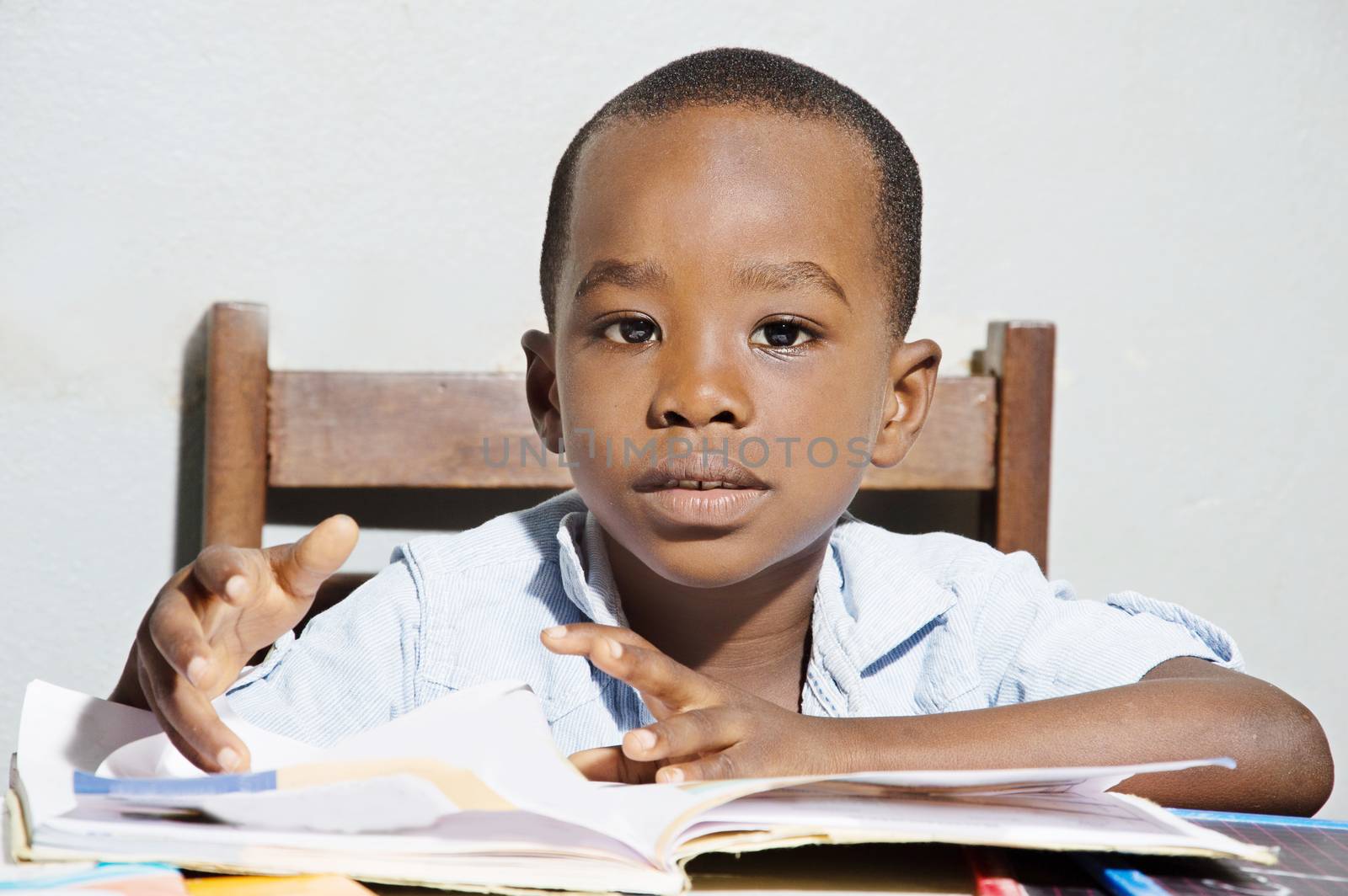 This child sitting on a chair , his reading book in front of him, looking in the camera objective.