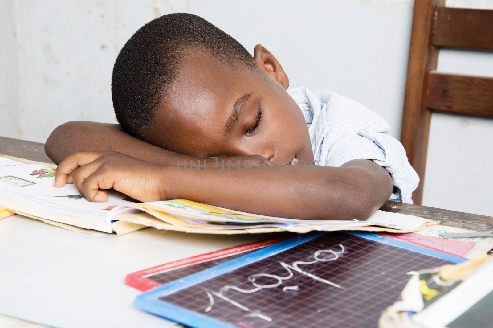 This child tired of studying , sleeping on his study table with his head in his book.
