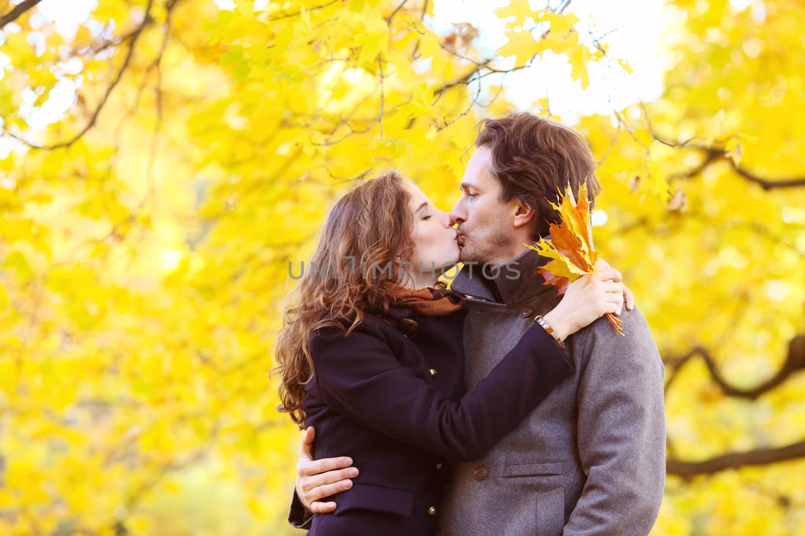 Happy couple kissing in autumn park with yellow trees